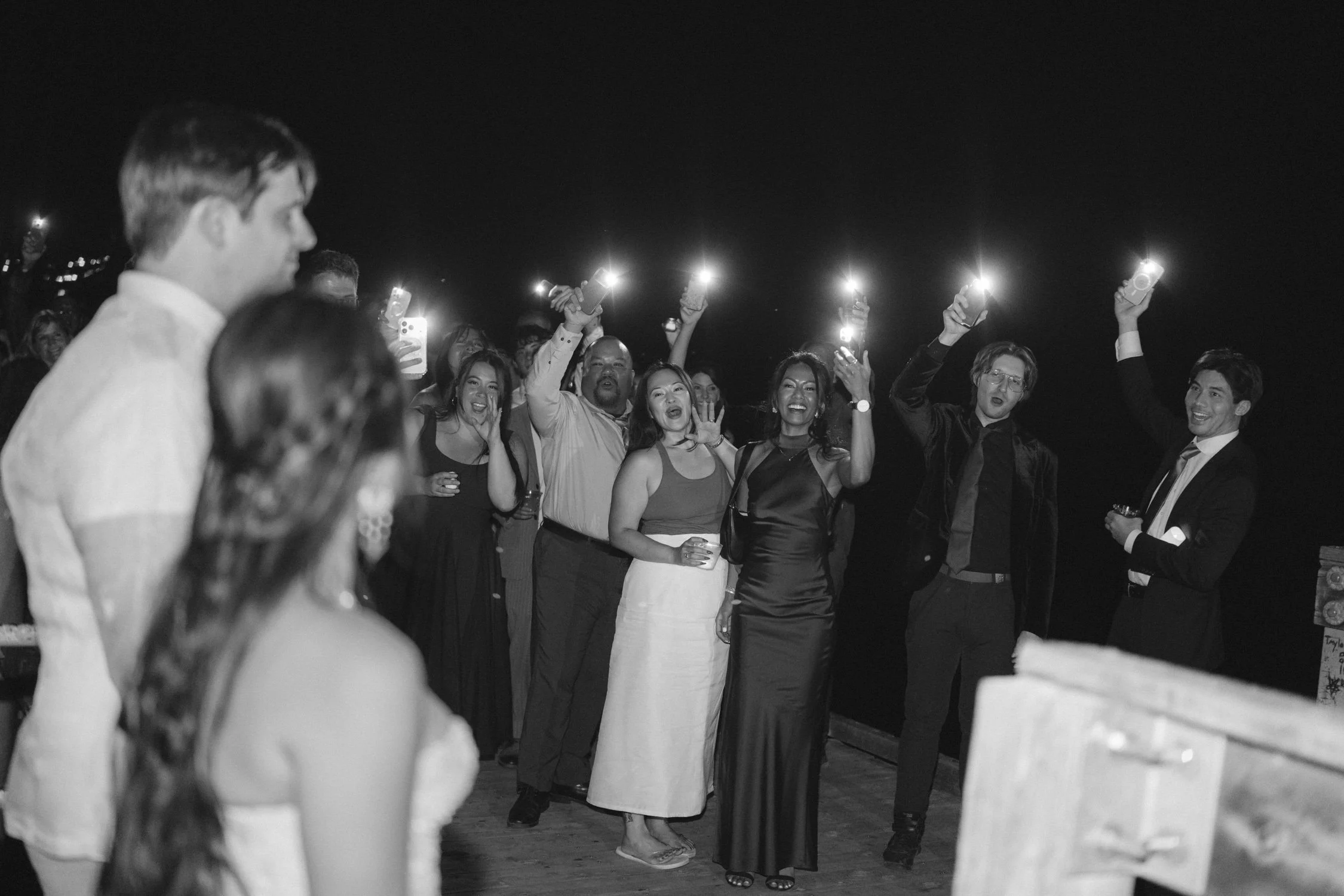 A Valhalla Lake Tahoe Wedding, photo of a nighttime wedding celebration where guests hold up lluminated flashlights to cheer for the newlywed couple