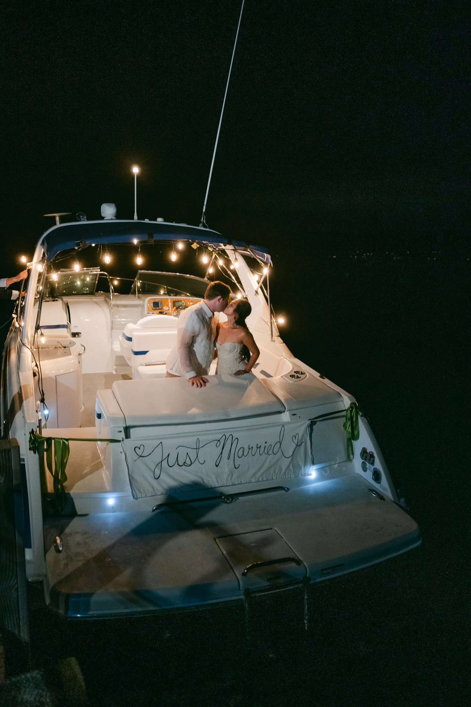 A Valhalla Lake Tahoe Wedding, photo of the newlywed couple kissing on the back of an illuminated motor yacht decorated with a "Just Married" banner
