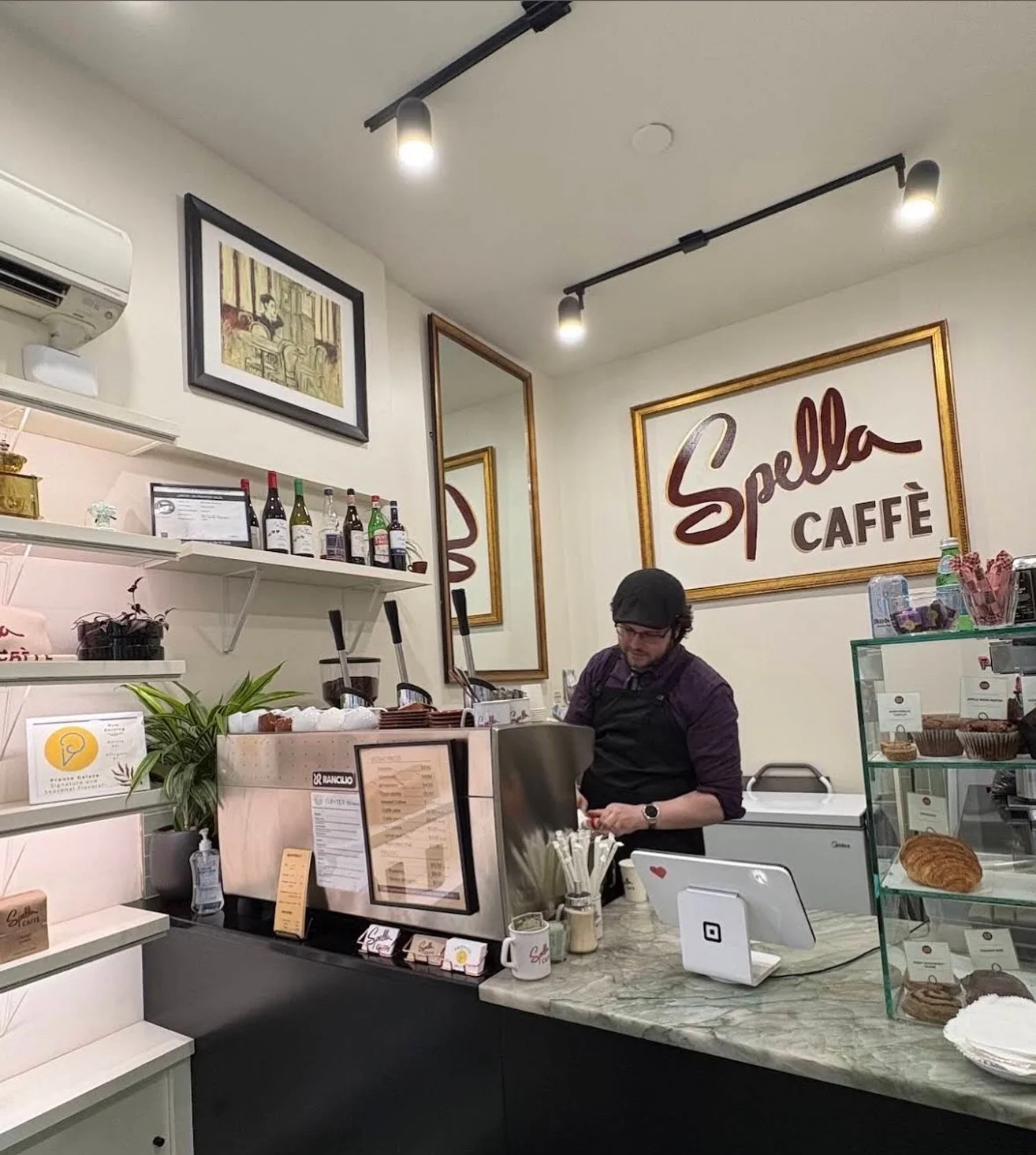 The morning rush is underway at Spella Caff&egrave;. Austin stands behind the lever espresso machine, lifting each lever with practiced confidence as customers gather at the bar. The aroma of freshly roasted coffee fills the room while cups clink ont