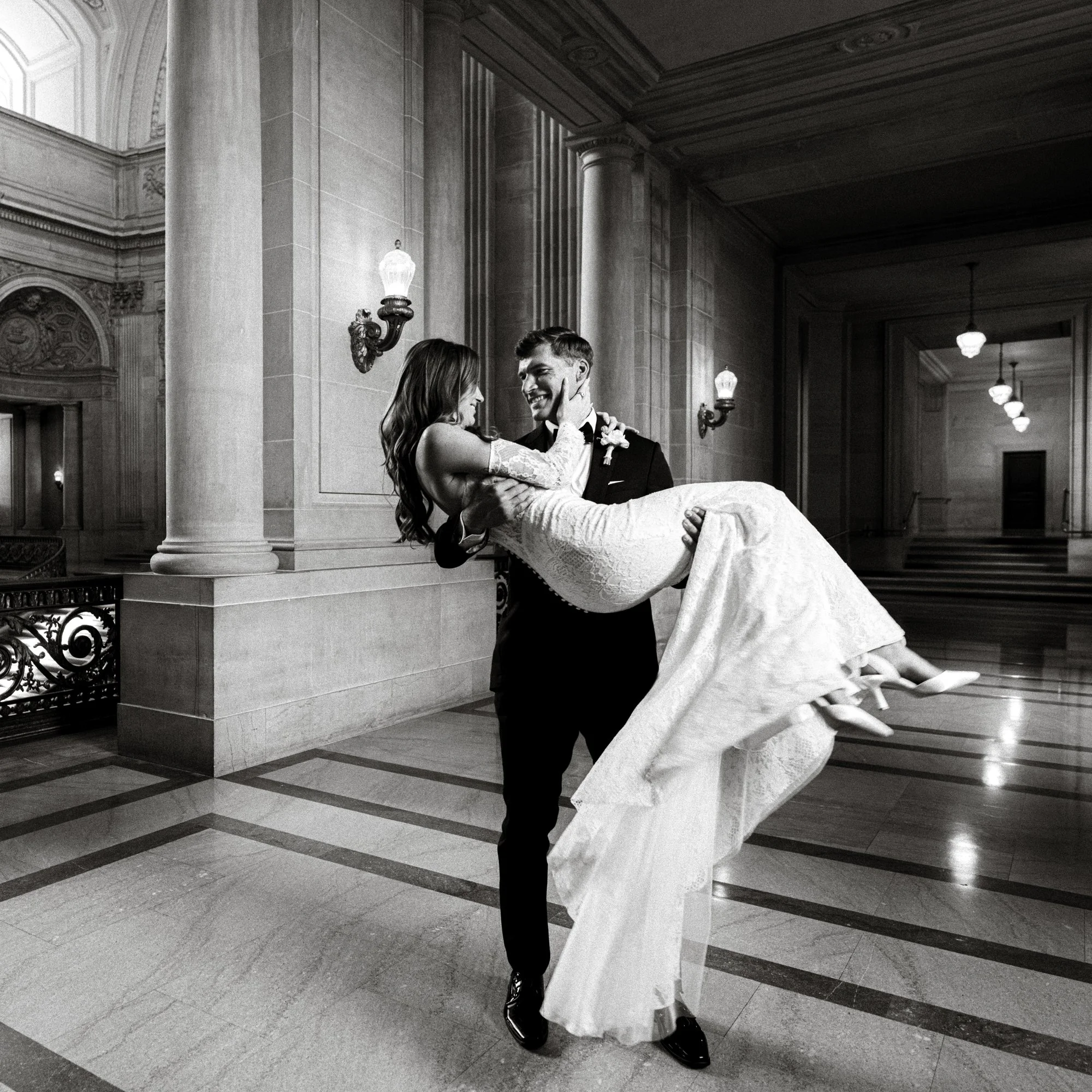 A groom carries his bride in a grand hall—perfect for a San Francisco City Hall wedding photographer to capture the elegance and love.