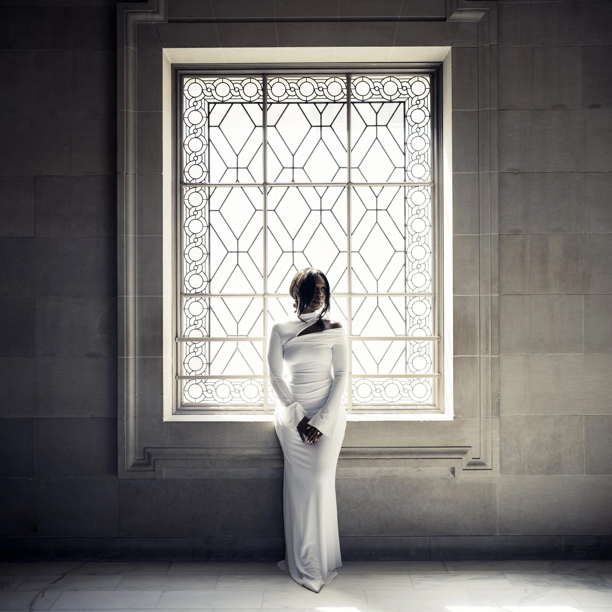 Elegant bride in a long white dress stands by an ornate window, softly lit—perfect scene for an sf city hall wedding photographer.