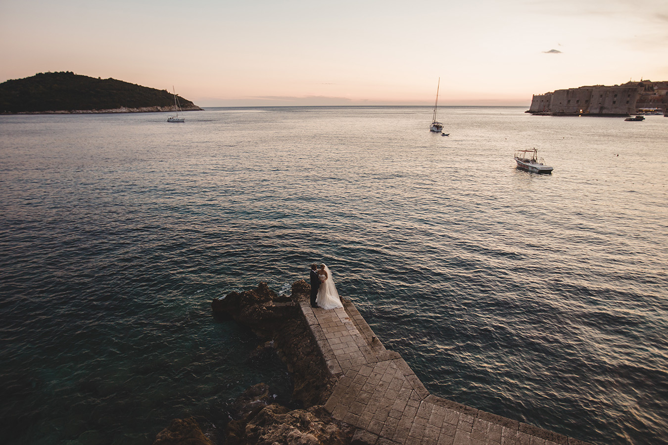 One of a set of images taken at this chic destination Wedding of Jenna & Nick. The stylish old town of Dubrovnik, Croatia.  The couple sit together by the water.  Photography by Matt Porteous