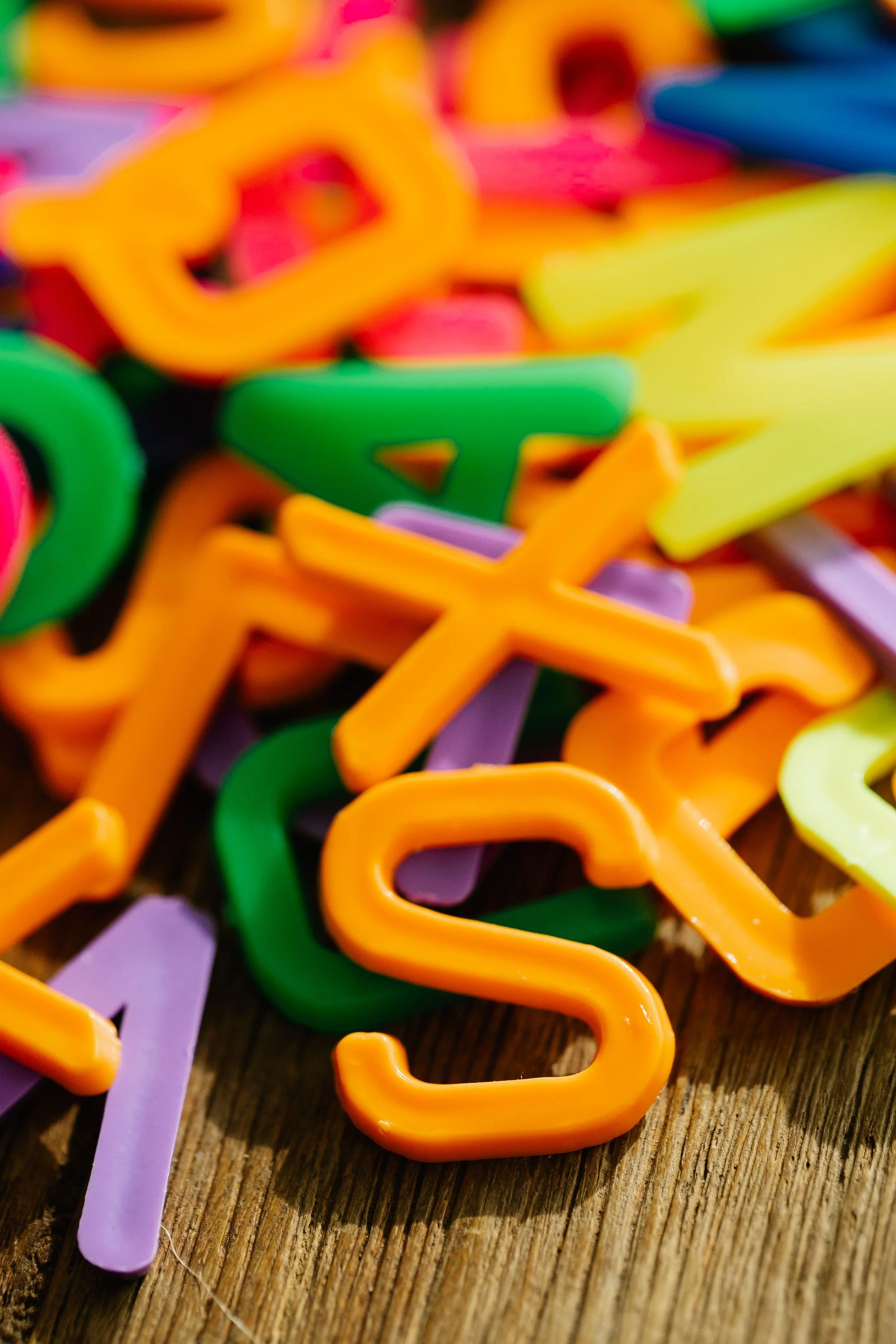Colorful plastic letters in orange, green, purple, yellow, and pink scattered on a wooden surface.