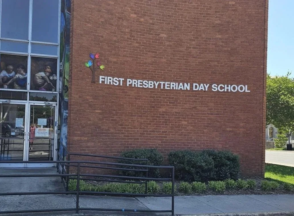 Exterior of First Presbyterian Day School building with a brick wall, the school name, and a colorful tree logo.