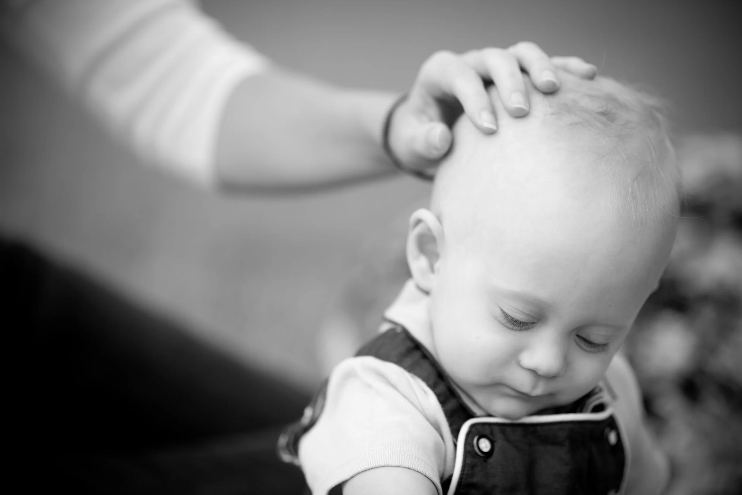 A child with a buzz cut receives a gentle head massage from an adult, with their eyes closed in a peaceful moment, in black and white.