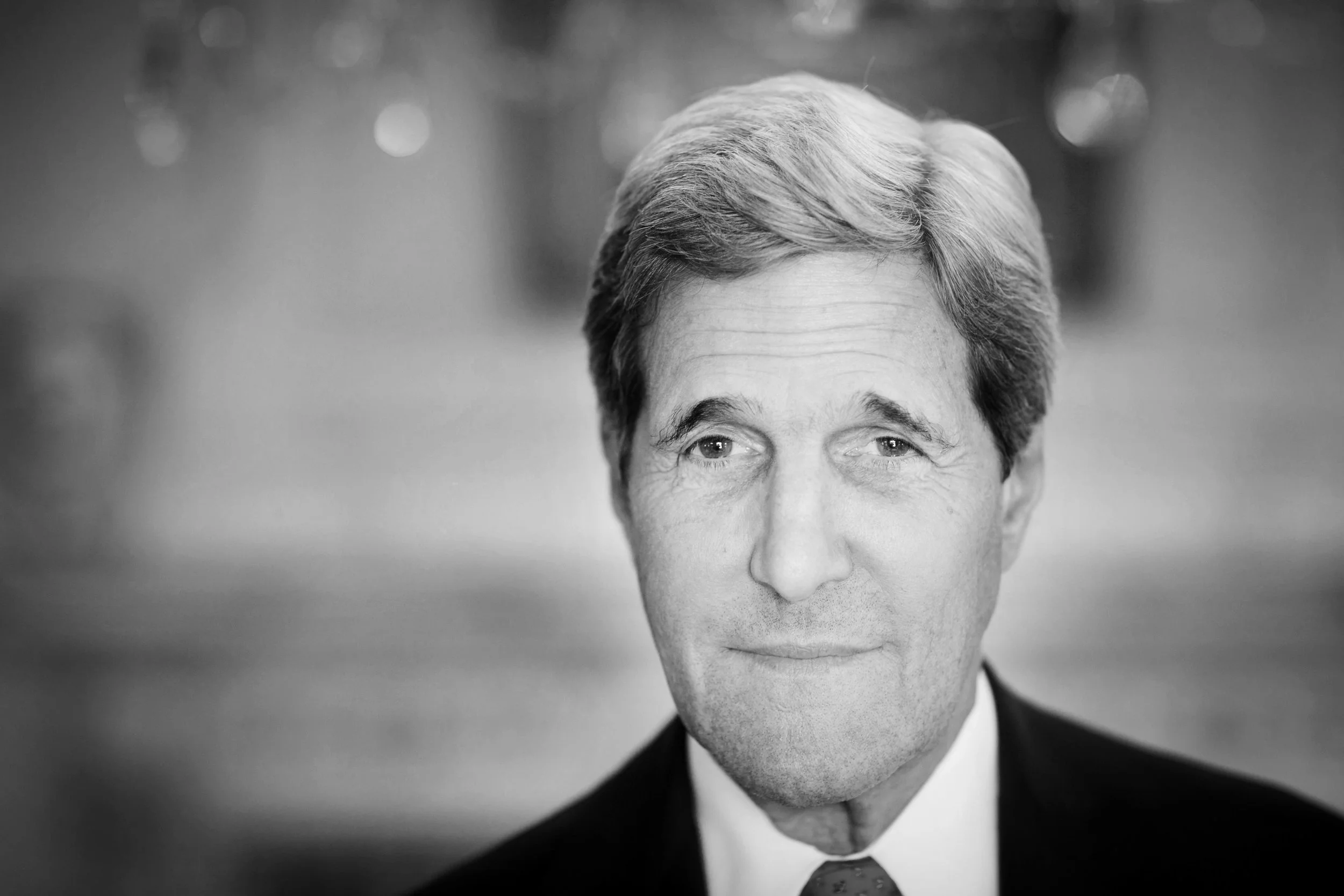 Black and white portrait of a middle-aged man with neatly combed hair, wearing a suit and tie, looking slightly to the right with a subtle smile.