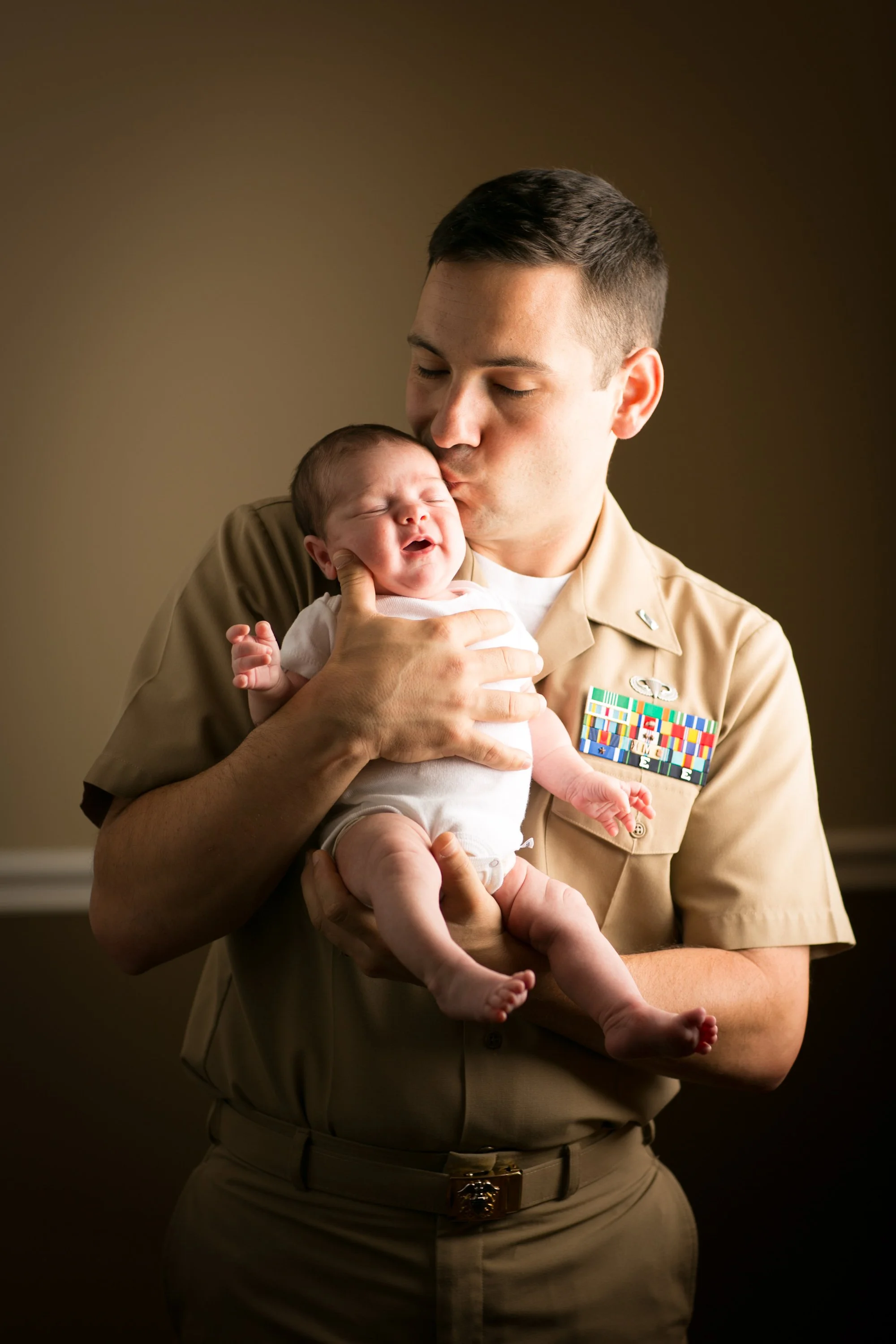 A man in a military uniform holding a crying baby in his arms.