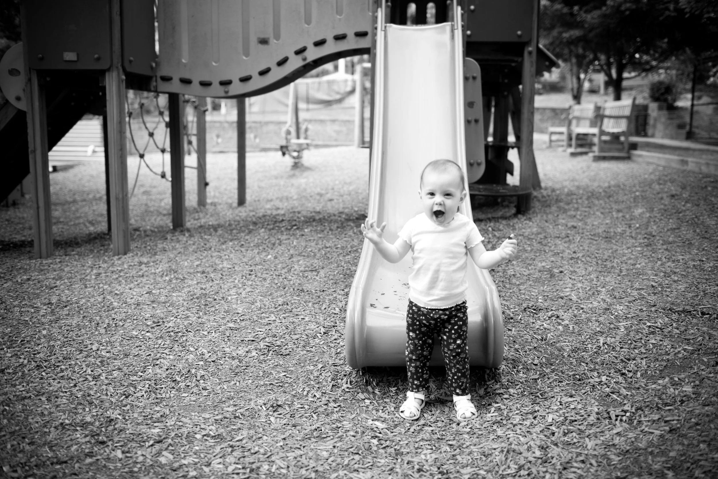 Child joyful at playground standing at the bottom of slide in black and white photo.