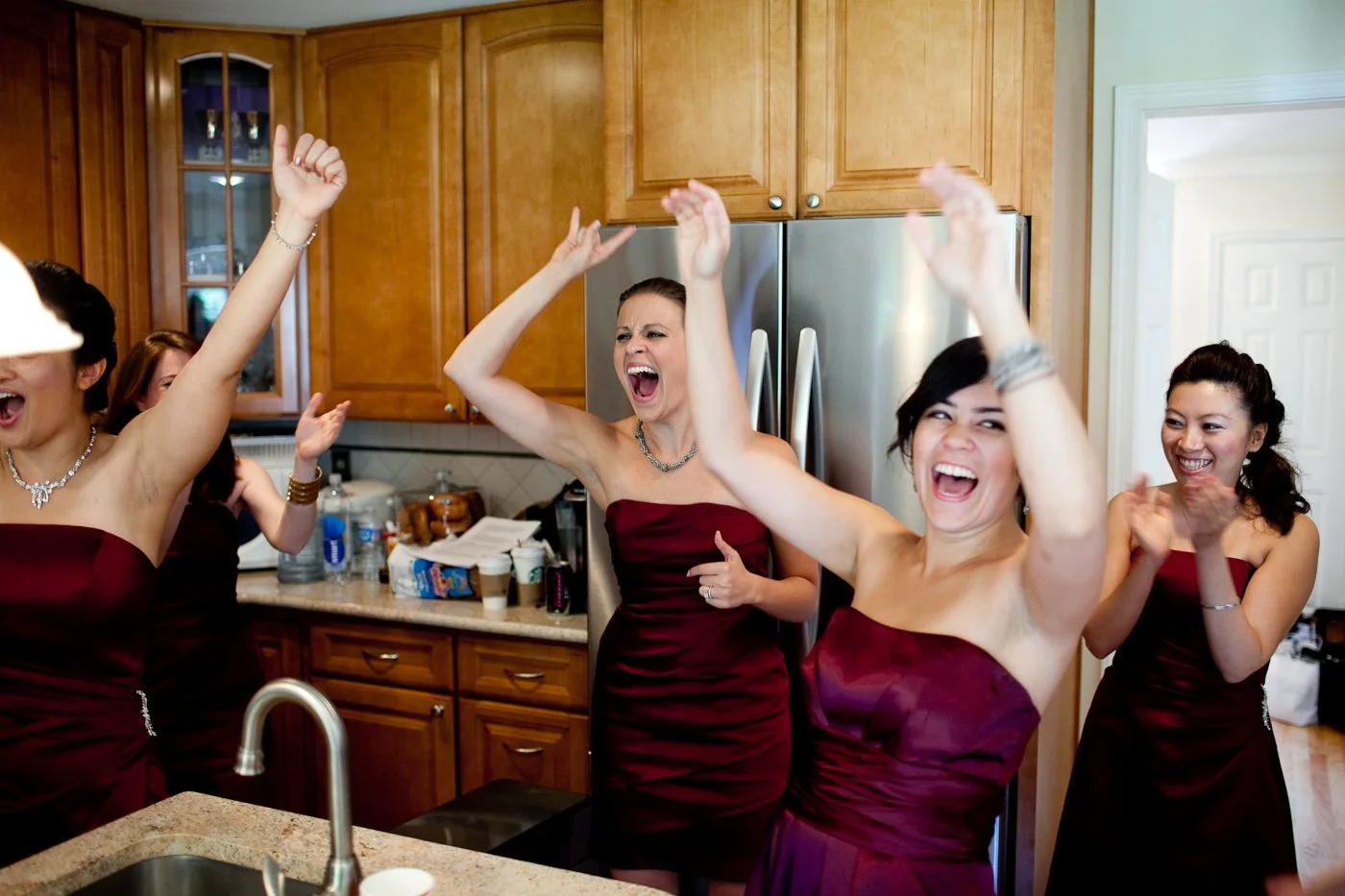 Women in burgundy strapless dresses celebrating and dancing in a kitchen.