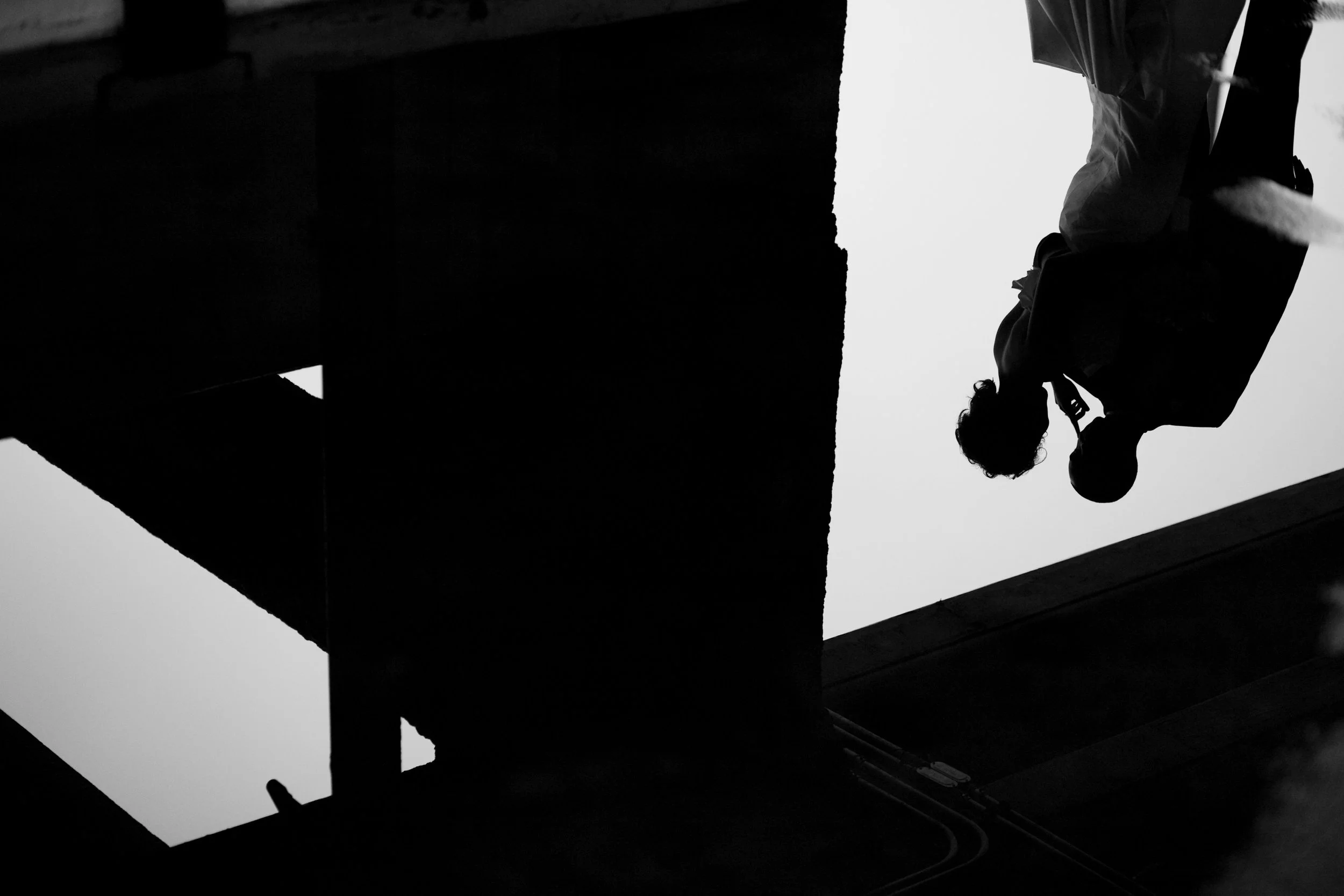 Silhouettes of two people, one with a backpack, standing outdoors against a bright sky, viewed from below.