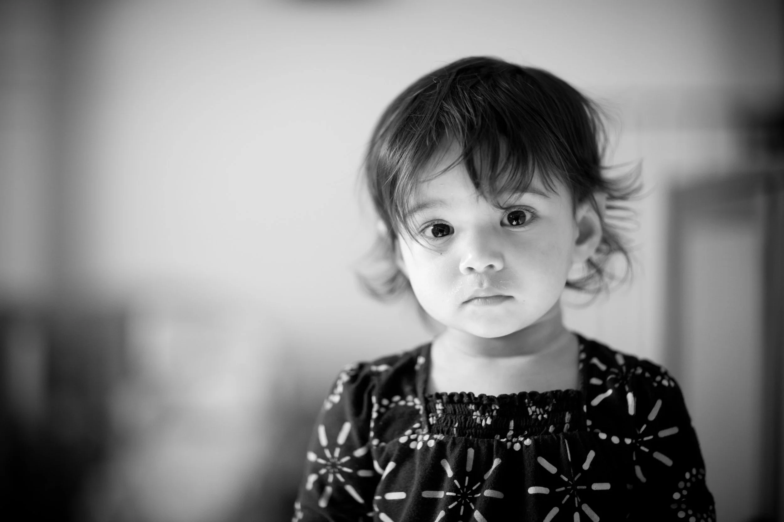 Black and white photo of a young girl with shoulder-length hair and large eyes, looking directly at the camera with a serious expression.