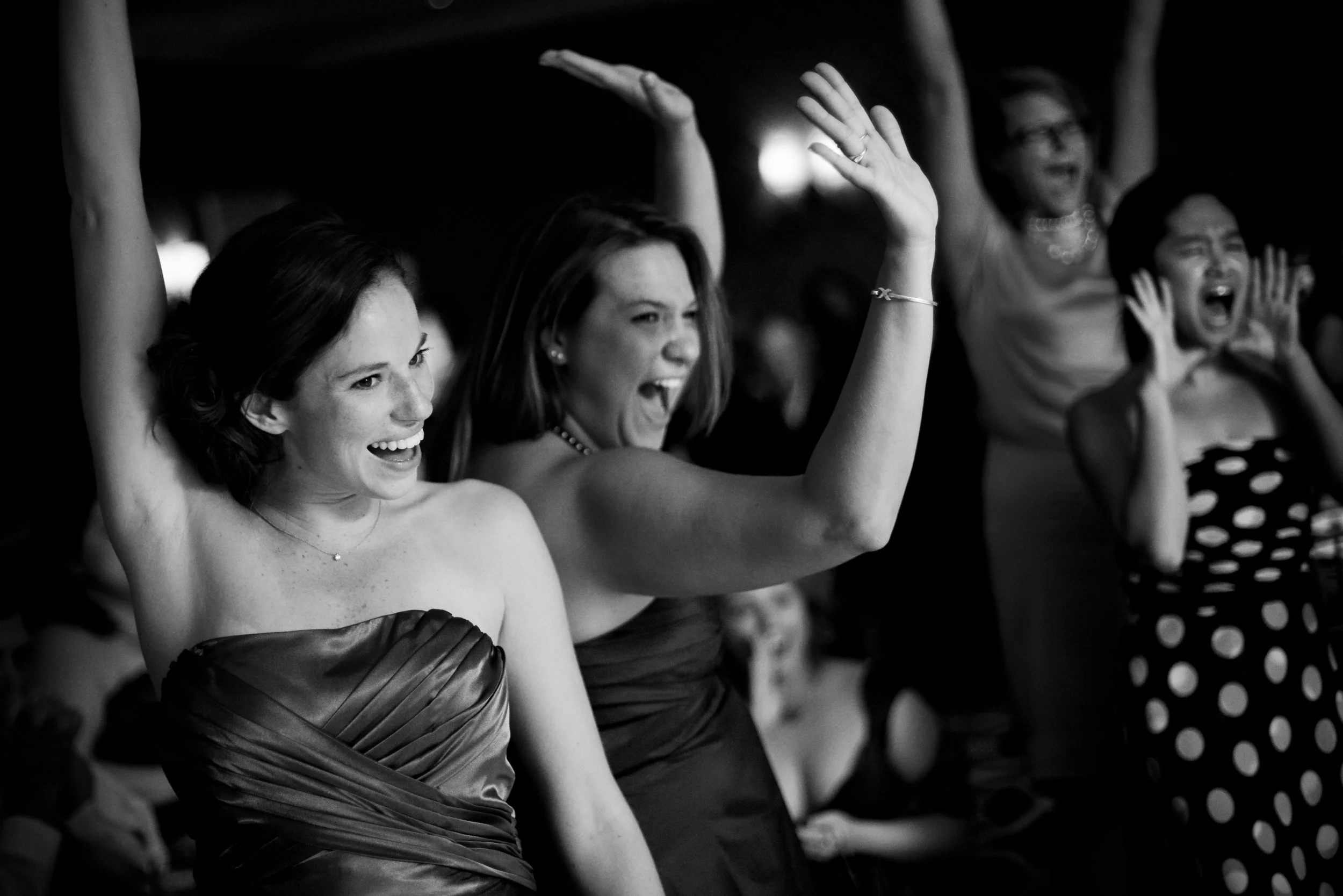 Group of women dancing and smiling at a lively event, captured in black and white.