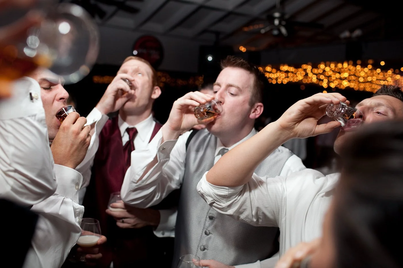 Group of men in formal attire drinking shots at a celebration or party.