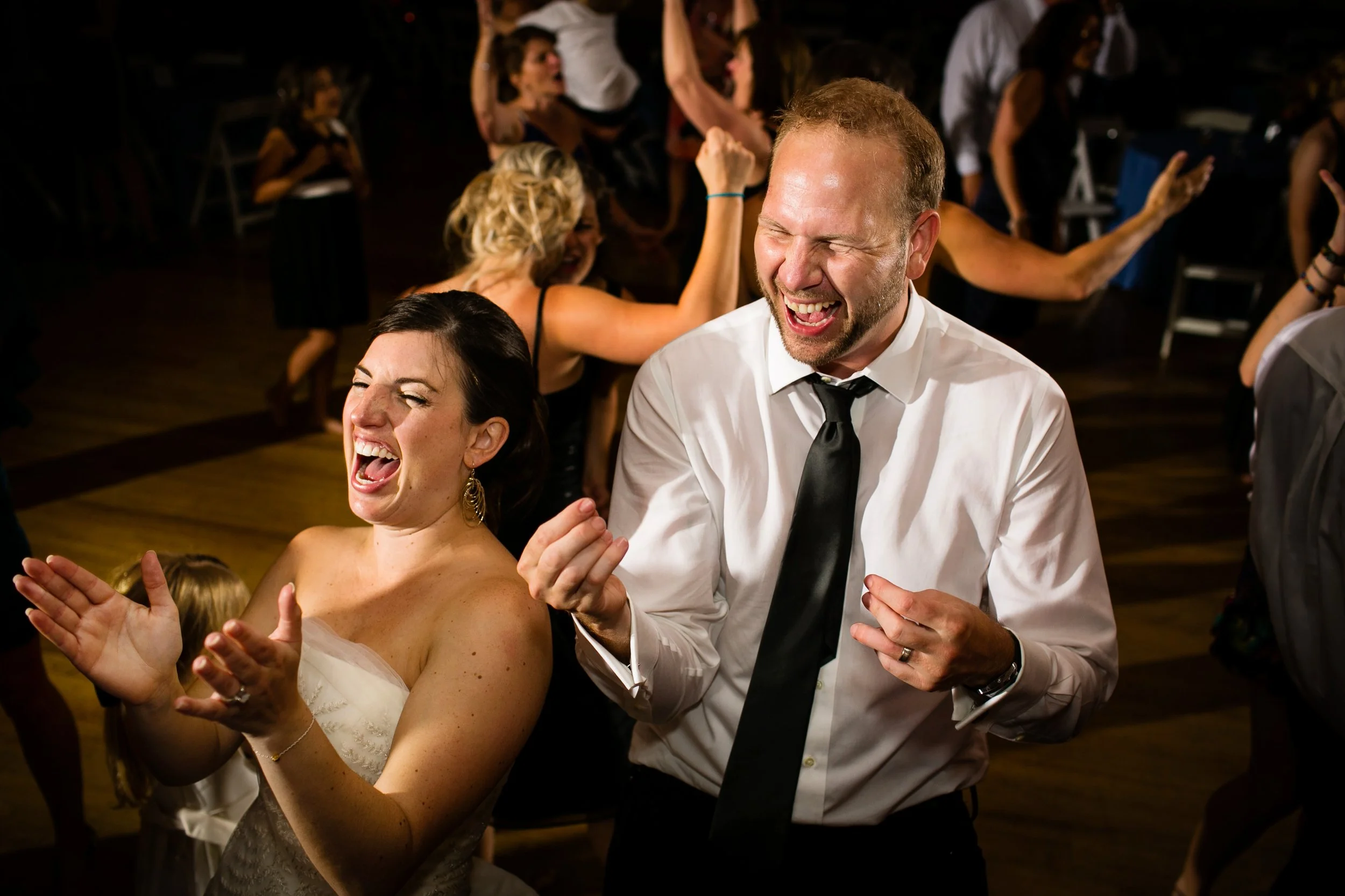 People dancing and celebrating at a party, with a woman in a wedding dress and a man in a white shirt and black tie in the foreground