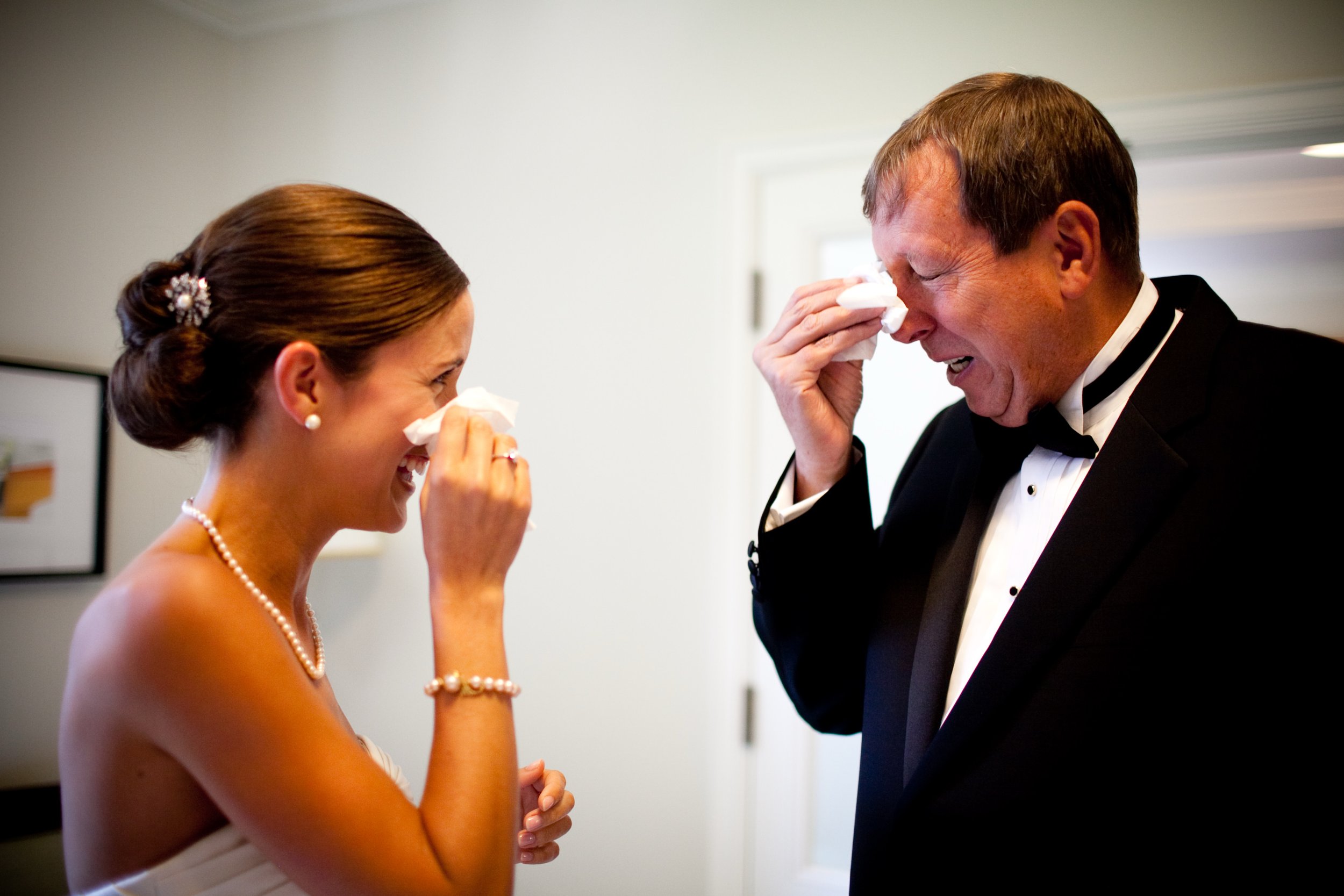 A bride and groom laughing and wiping tears of joy on their wedding day.
