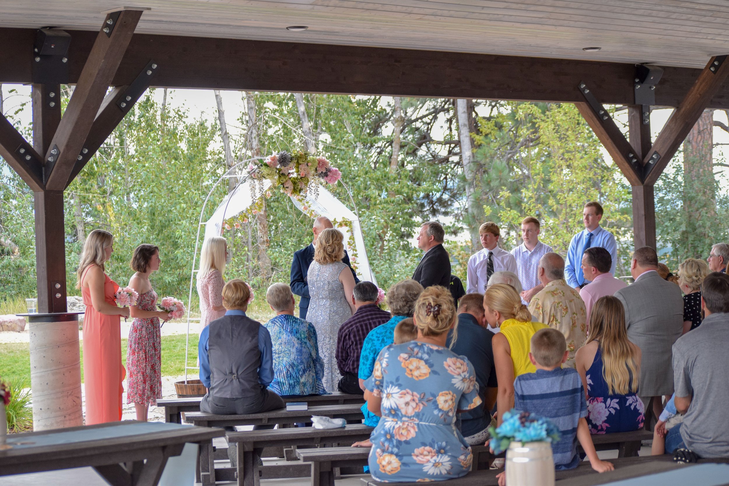  a wedding taking place underneath of the pavilion. A white alter covered in flowers with a bride dressed in blue and a groom in a black suit 