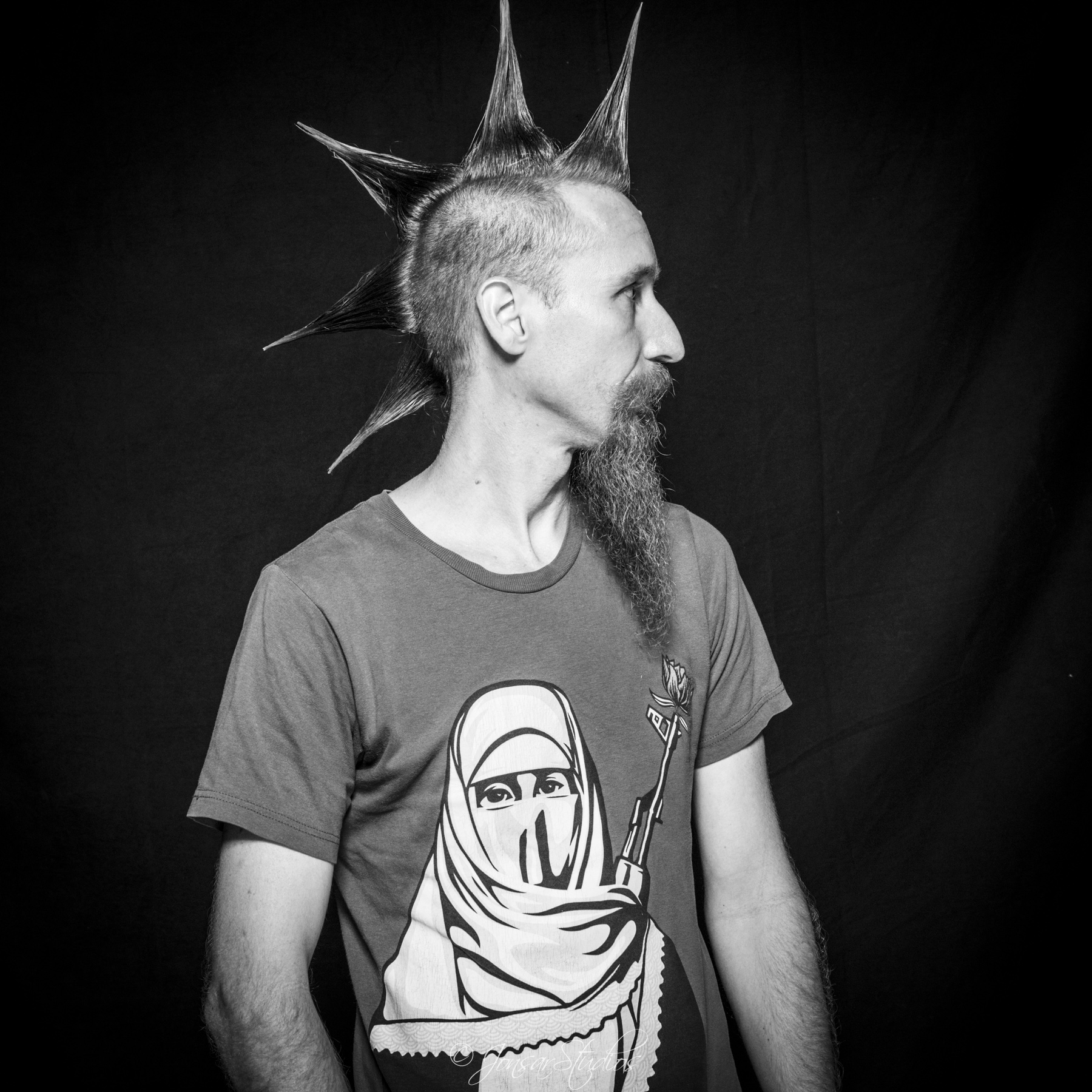 Profile of man with spiked mohawk and gun teeshirt, photographed on black background