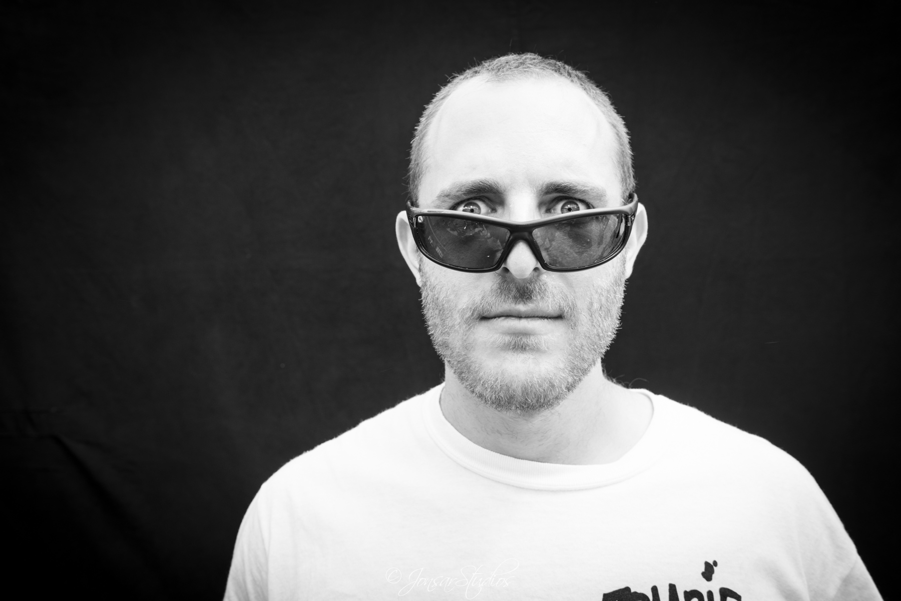 Portrait of man peering over sunglasses, photographed on black background