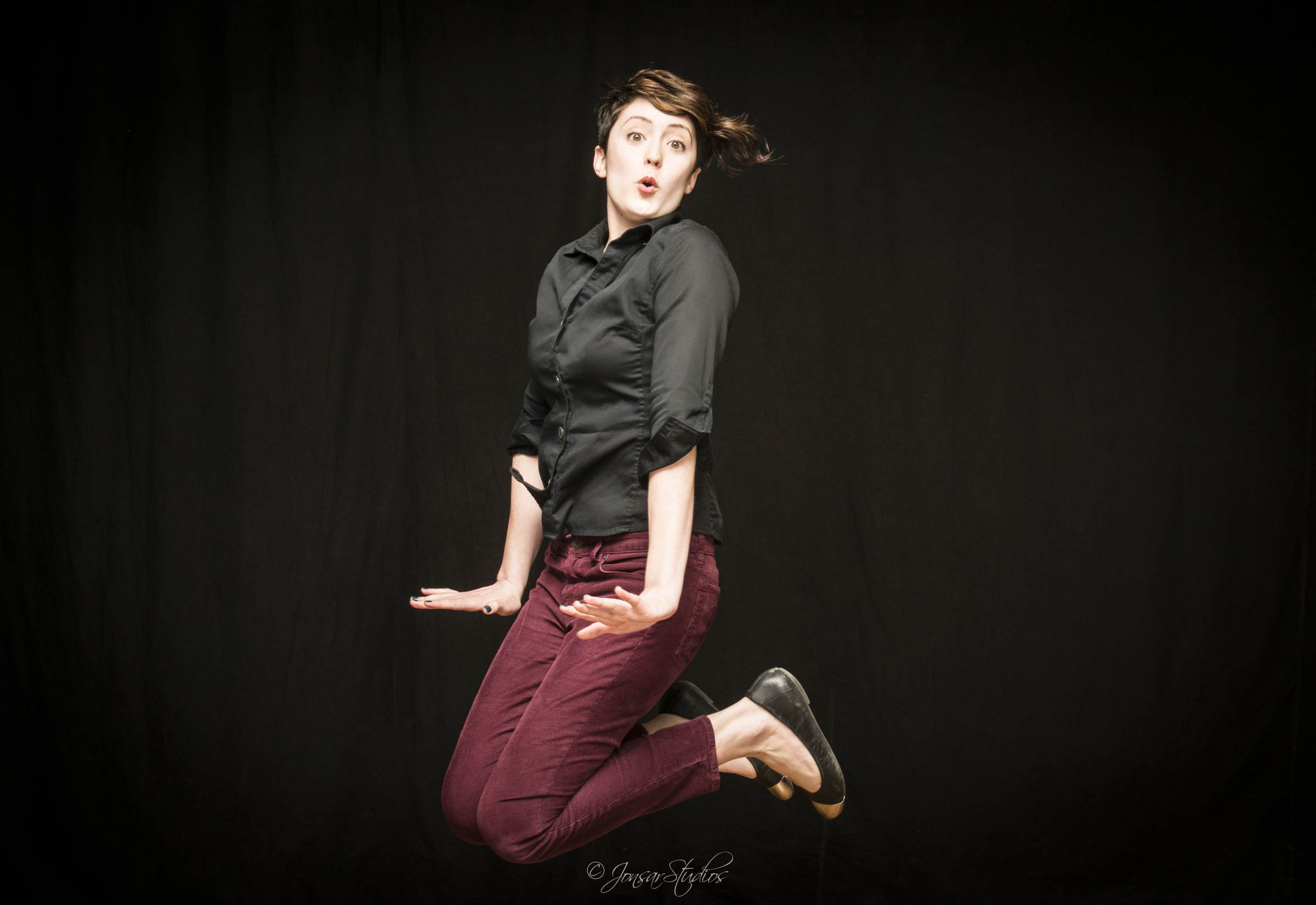 Portrait of Young Woman wearing Red Pants jumping in air on black background