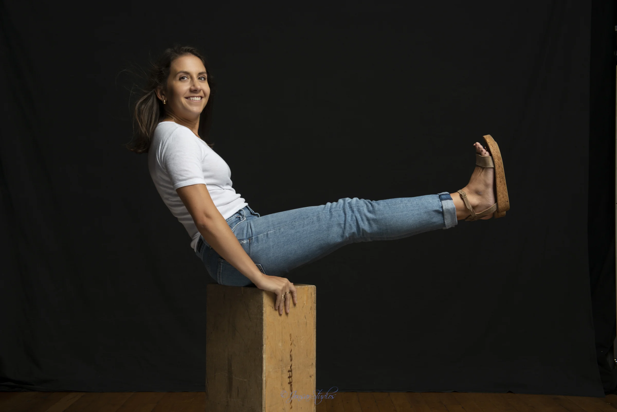 Color studio portrait of woman in jeans on apple box on black backdrop