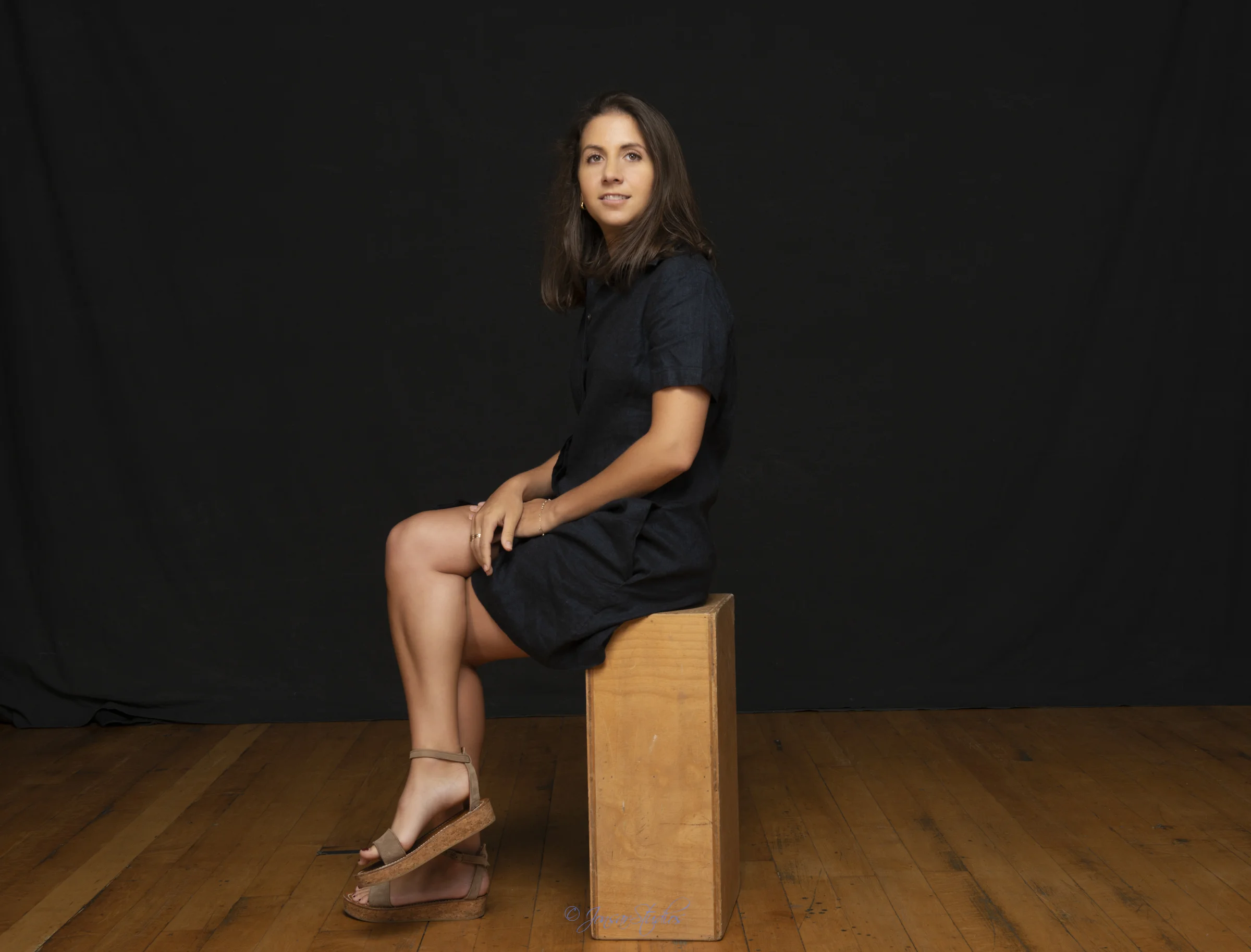 Color studio portrait of woman seated on apple box on black backdrop