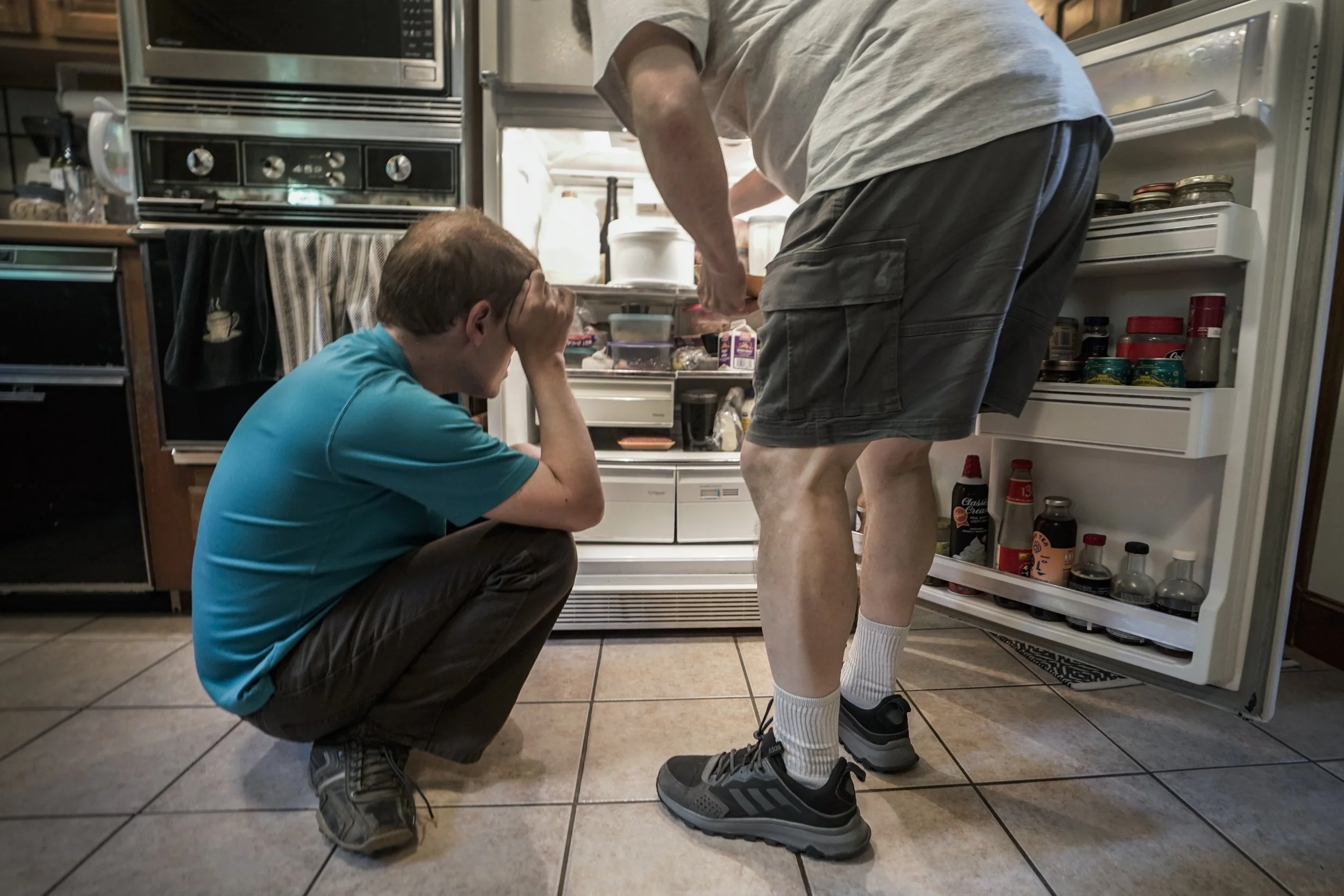  Andy Tranfaglia covers his face while squatting near the refrigerator as his father Mike Tranfaglia looks for food to prepare for Andy's dinner.  