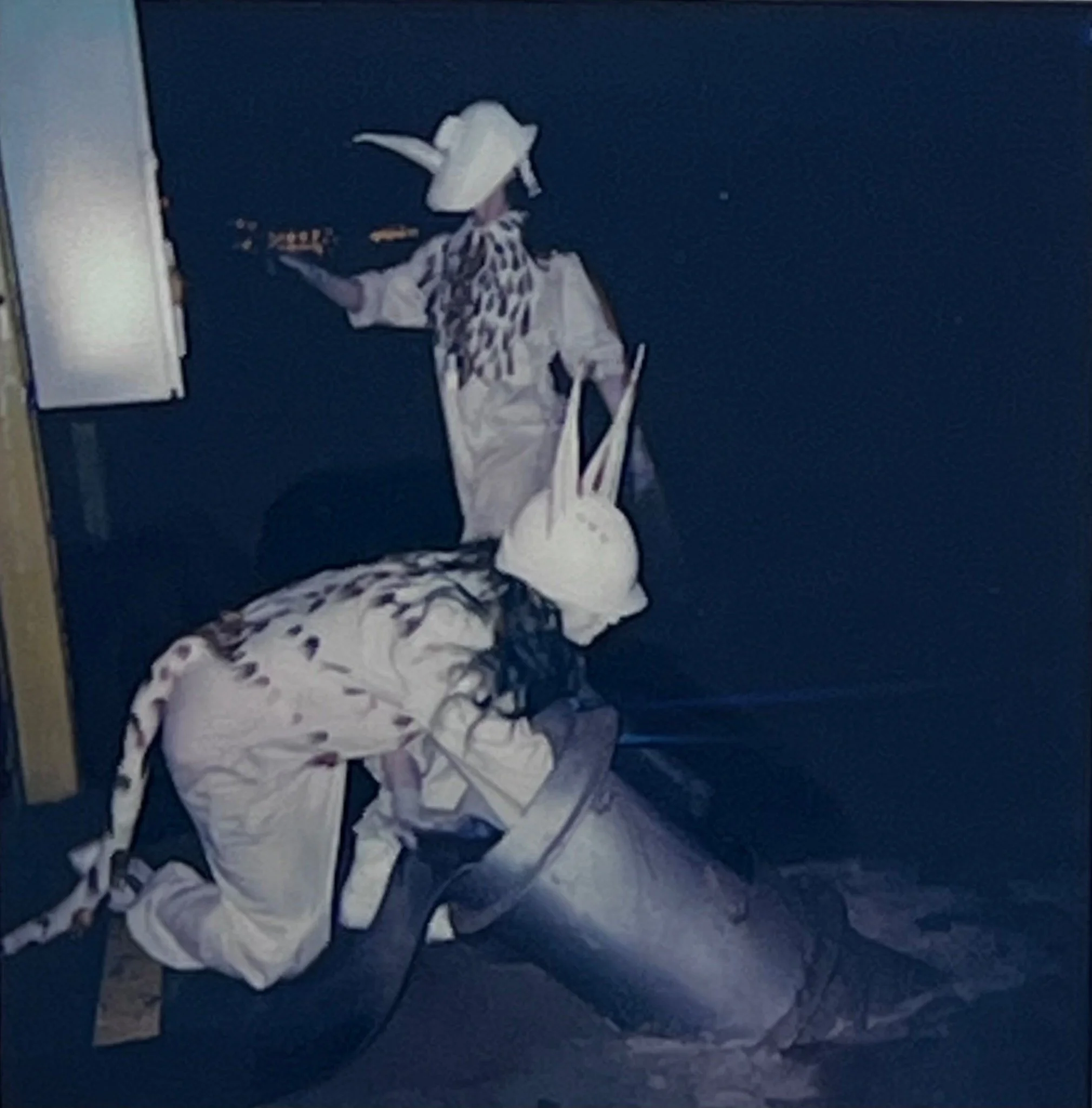 One performer bends across a metal cylinder while another stands and points into the dark factory space.