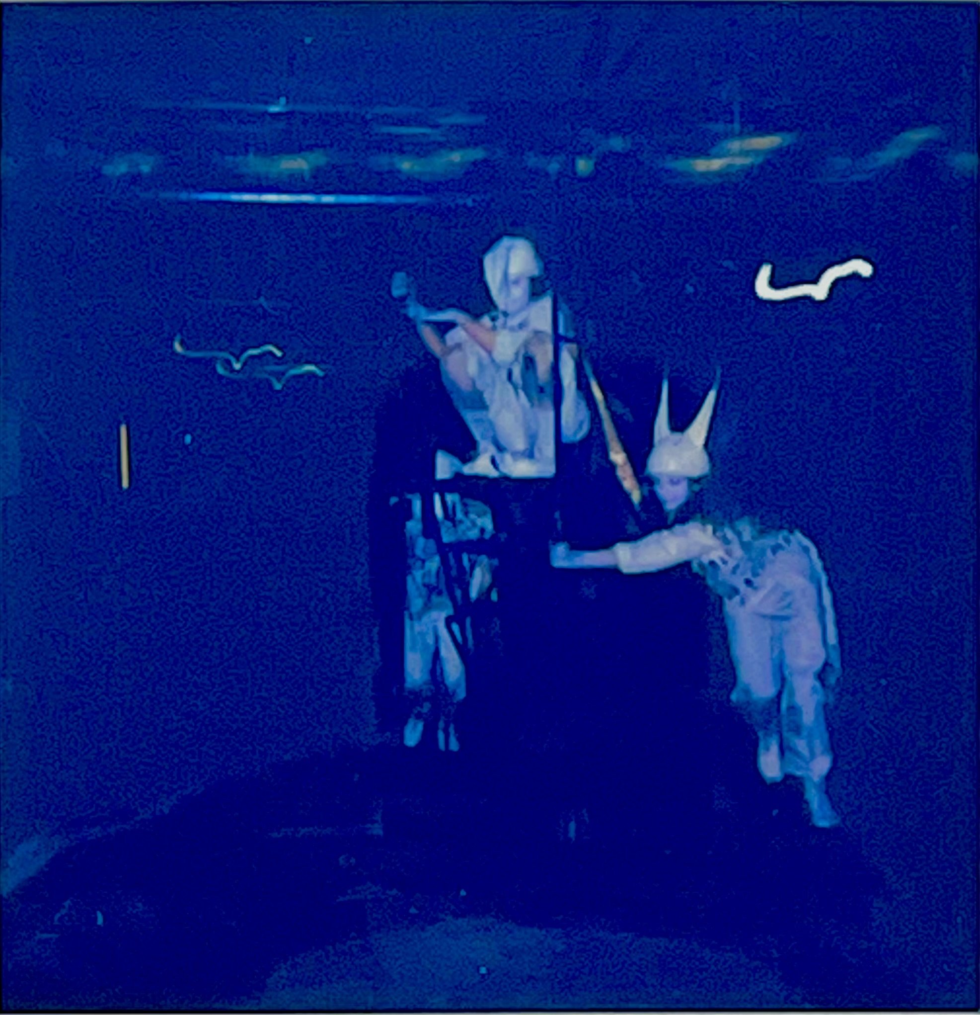 Blue-toned Polaroid of two performers gathered at an industrial machine, one raised above the other.