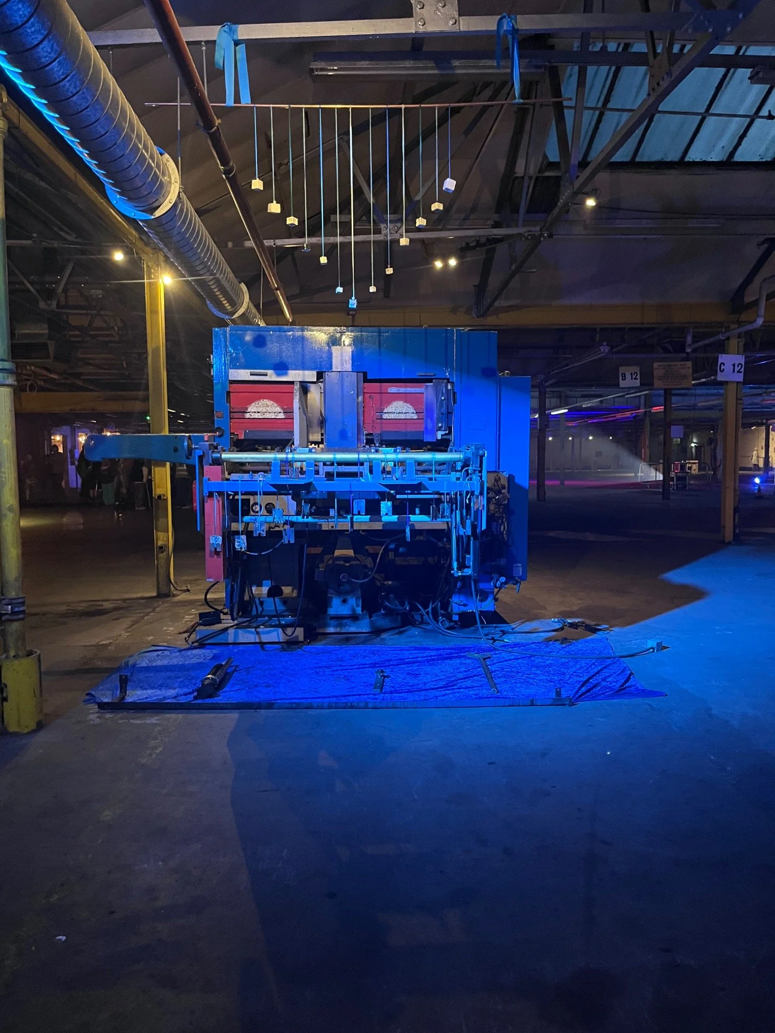 A decommissioned blue factory machine beneath suspended ceramic forms and blue ribbons.