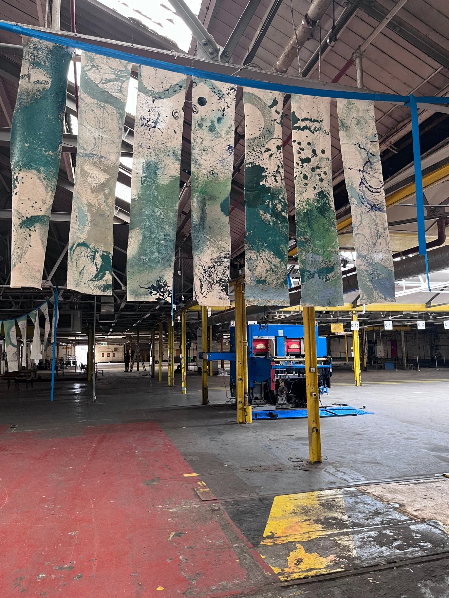 Collaborative painted banners suspended above a decommissioned blue machine inside The Paper Factory.