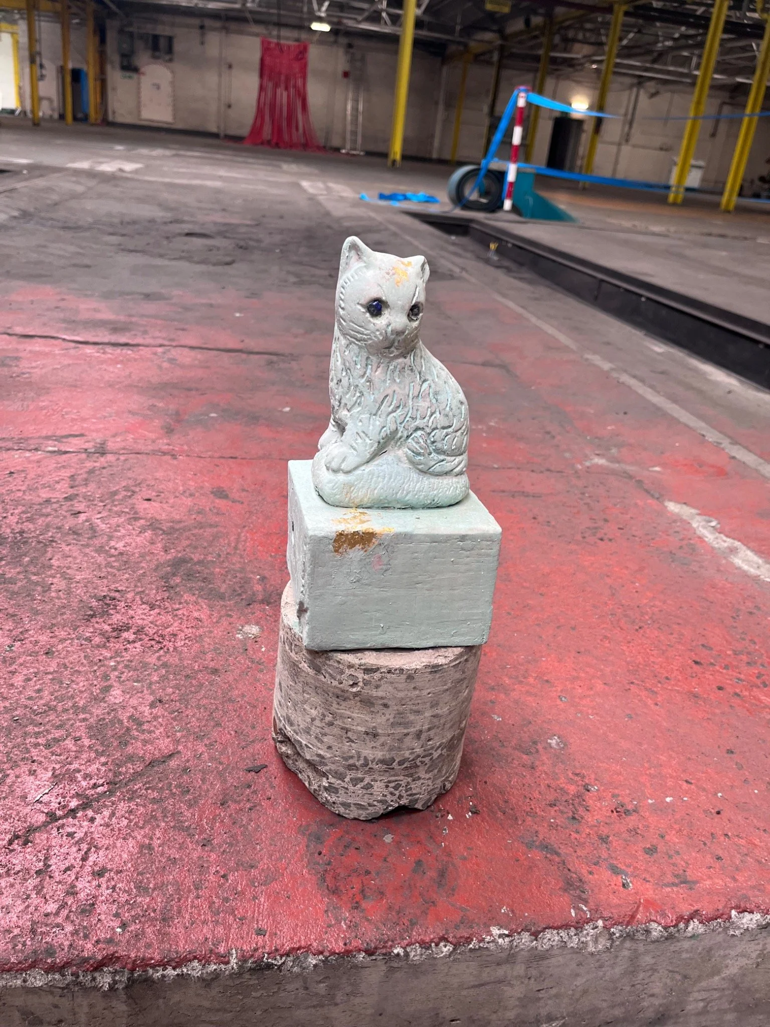 A small ceramic cat displayed on a ceremonial plinth within the factory installation.