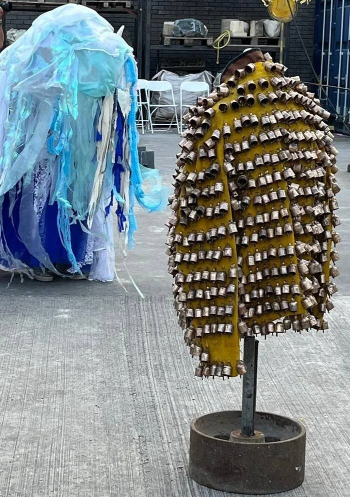 A blue and white jellyfish costume beside an ochre sculptural garment covered with small cast objects for Sea Fallen Stars.