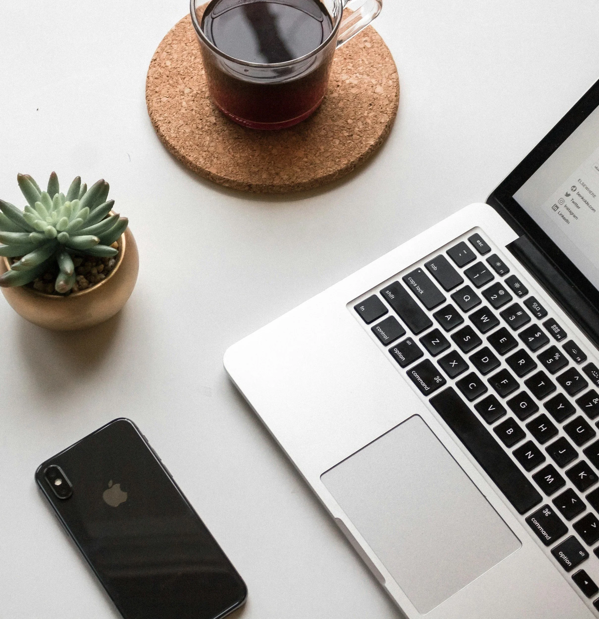 Laptop, Smartphone, Kaffee und kleine Pflanze auf dem Tisch – Einladung zur Online‑Buchung der Interior‑Design‑Beratung