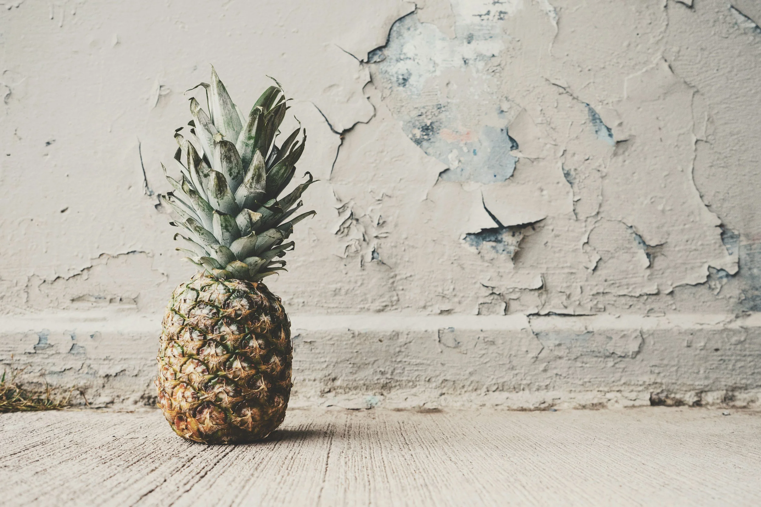 Einzelne Ananas vor heller Wand auf Holzoberfläche – Symbol für Pinatex und andere vegane Alternativen zu klassischem Leder.