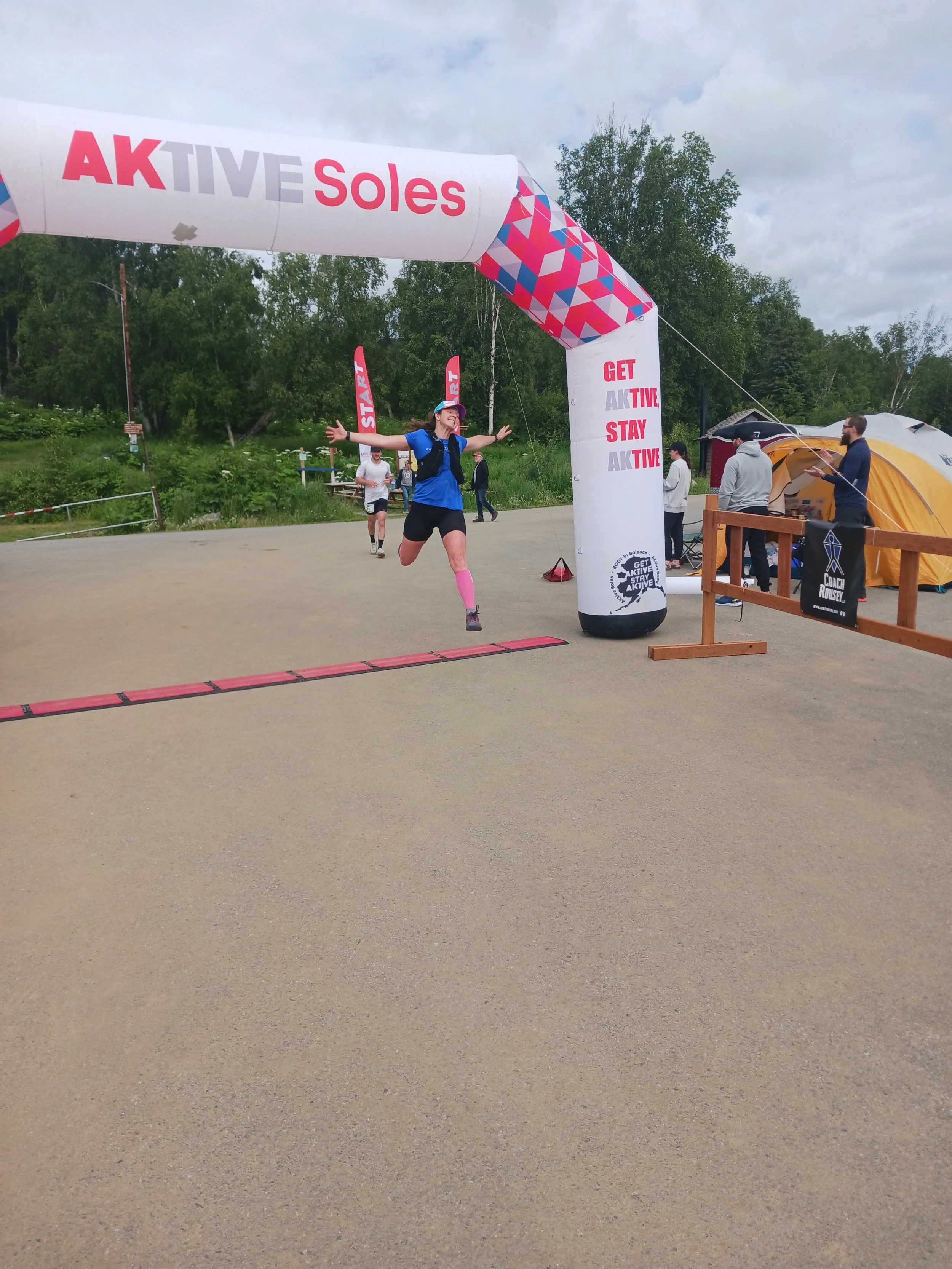 Amy Bushatz finishing a Backyard Ultra, smiling at the finish with spectators behind her.