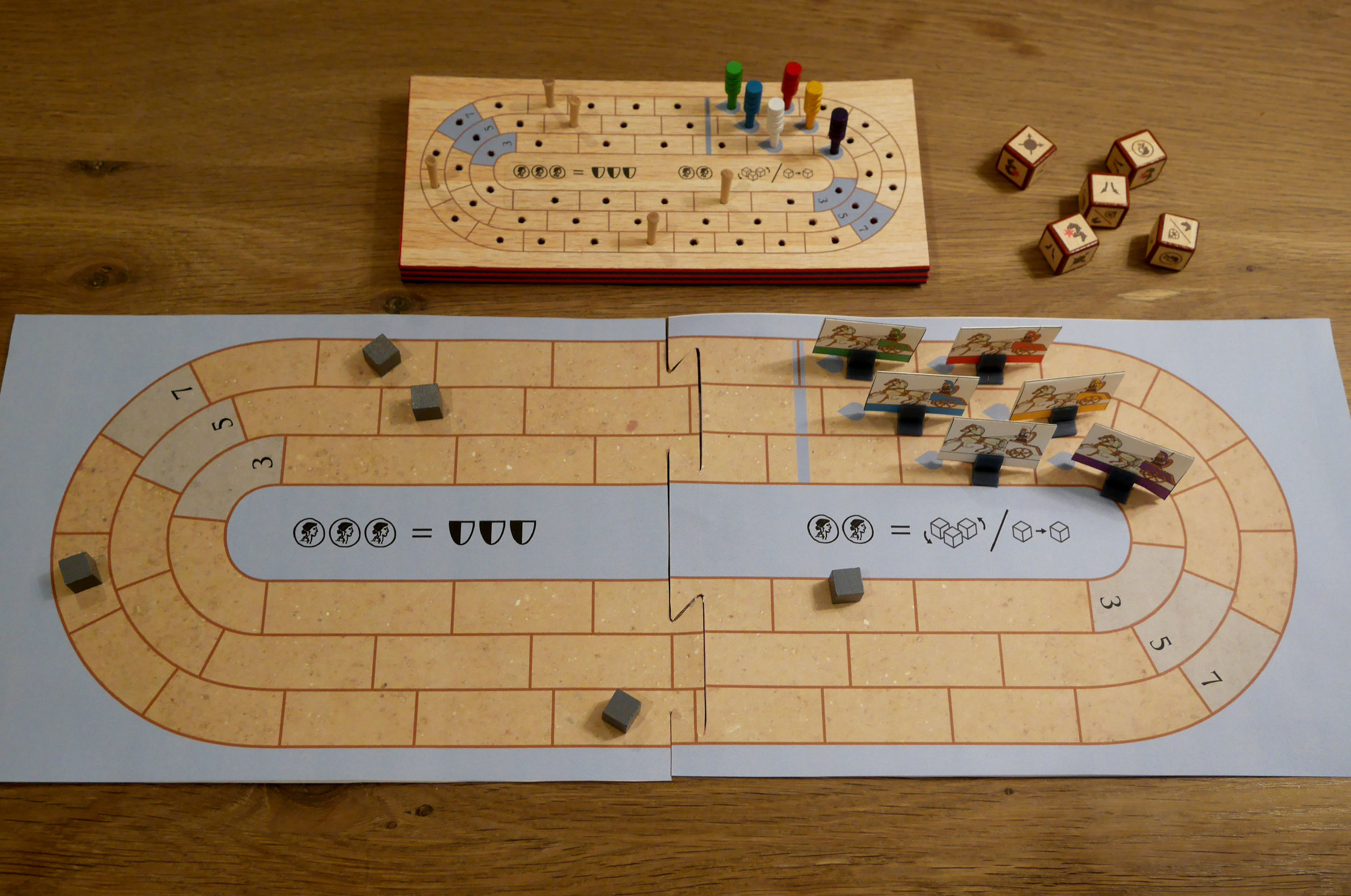 This is one of the "wood" prototypes (made from foam) alongside the board game version. Moving to more traditional materials cut the game's cost by more than half and opened up the possibility of including a double-sided board and variable chariots. The wood was fun but terribly expensive and the chariots (as cribbage pegs) weren't very thematic.