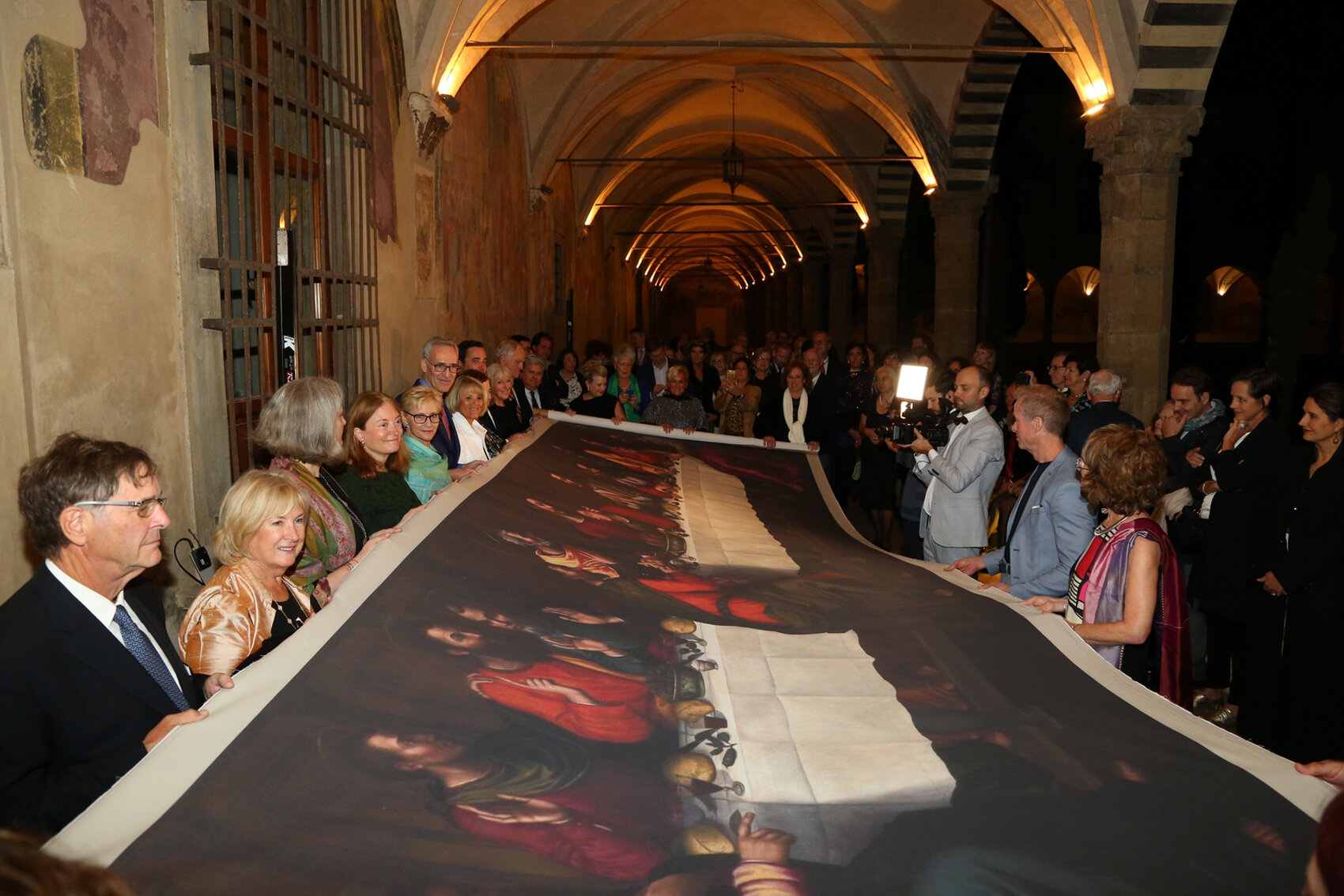  AWA patrons at the Cloister of Santa Maria Novella celebrate the unveiling of Nelli’s Last Supper by unrolling the ‘life-size’ replica, as a gift to the Dominican Community. (Ph. S. Silvia) 