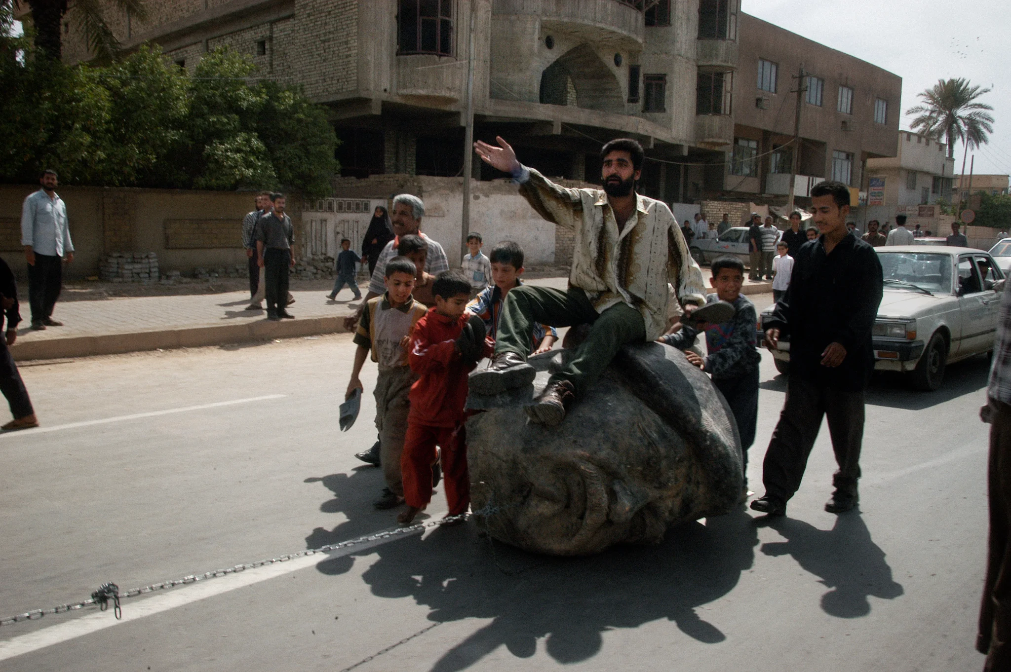 Baghdad, Iraq April 18, 2003 Iraqis ride a head of Saddam Hussein being dragged by a truck. They are also beating it with shoes, which is considered to be the most insulting gesture in Iraqi society. Photograph by Alan Chin