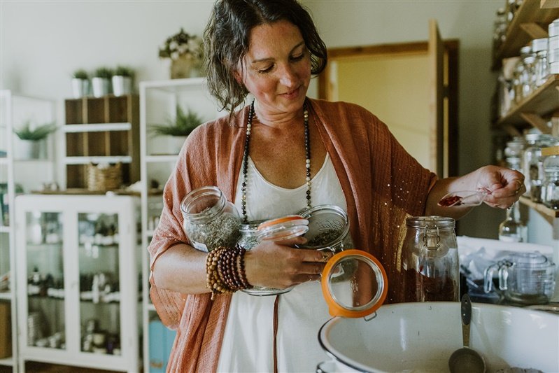 Woman in a kitchen holding spice jars and scooping from a jar