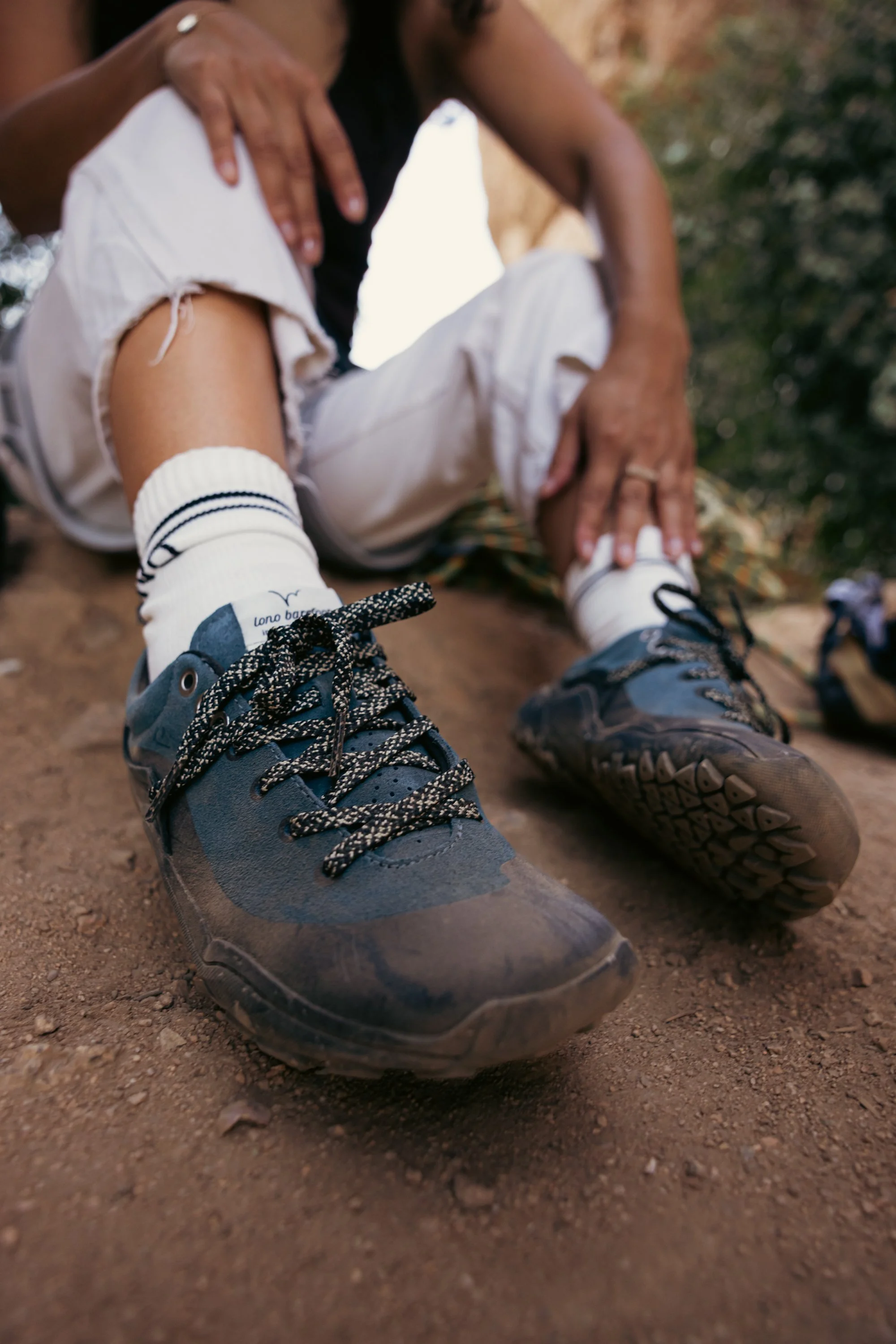 A person tying the laces of hiking shoes while sitting outdoors on a dirt trail. Rock climbing shoe brand photography.