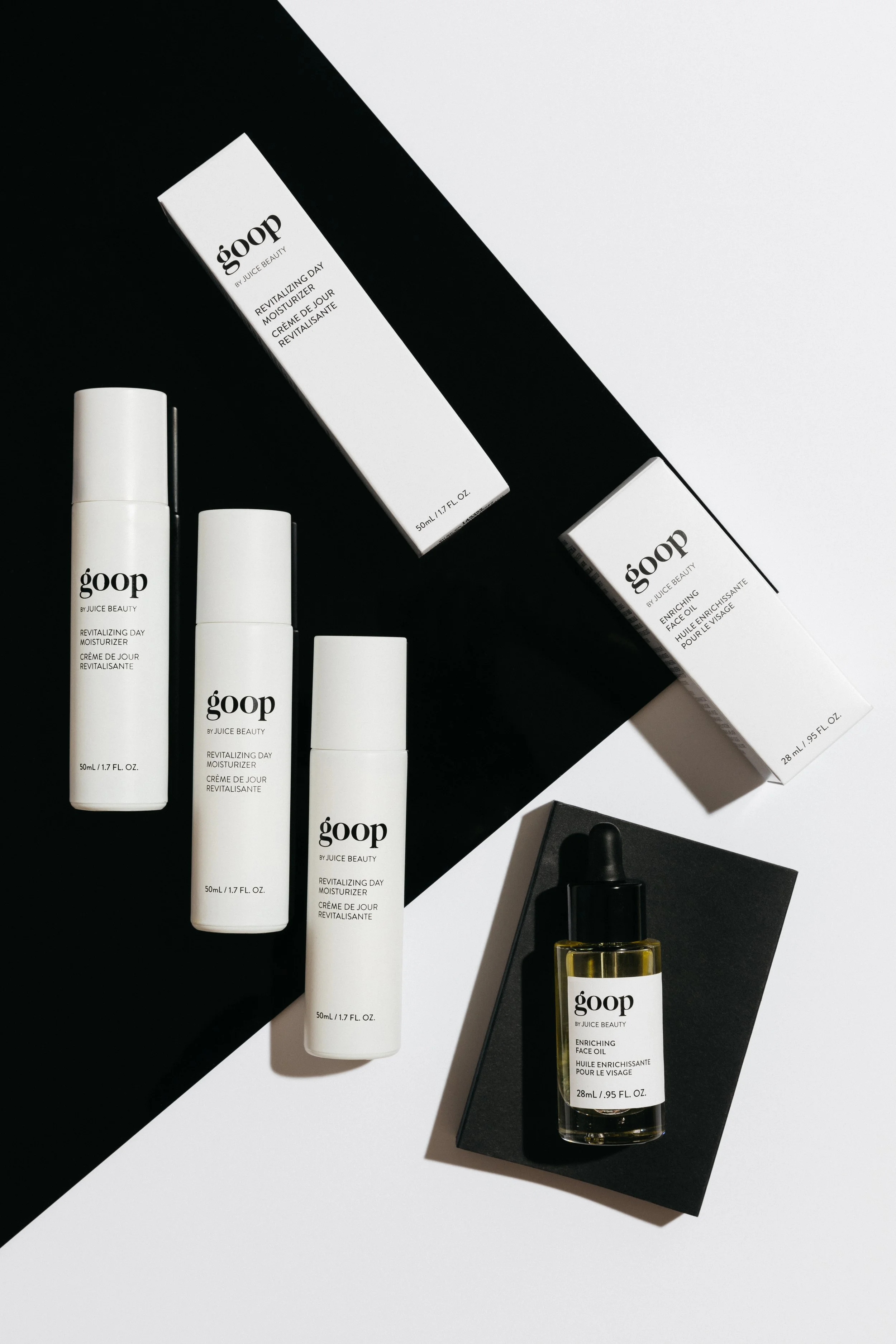 Collection of skincare products including three bottles of goop by Juice Beauty revitalizing day moisturizer, two boxes, and a bottle of enriching face oil with dropper, arranged on a black and white background.