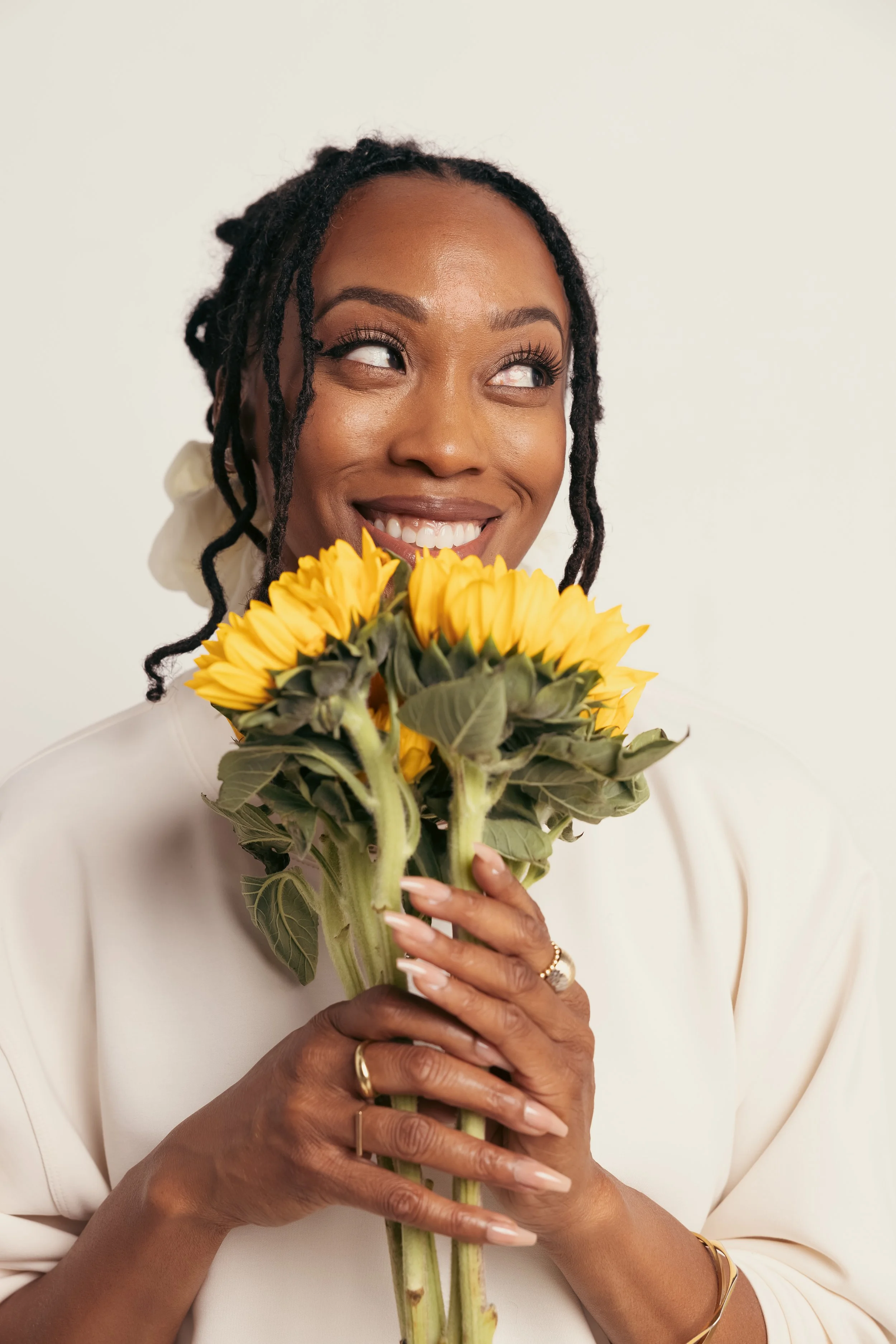 Woman  holding a bouquet of sunflowers and smiling with white teeth.