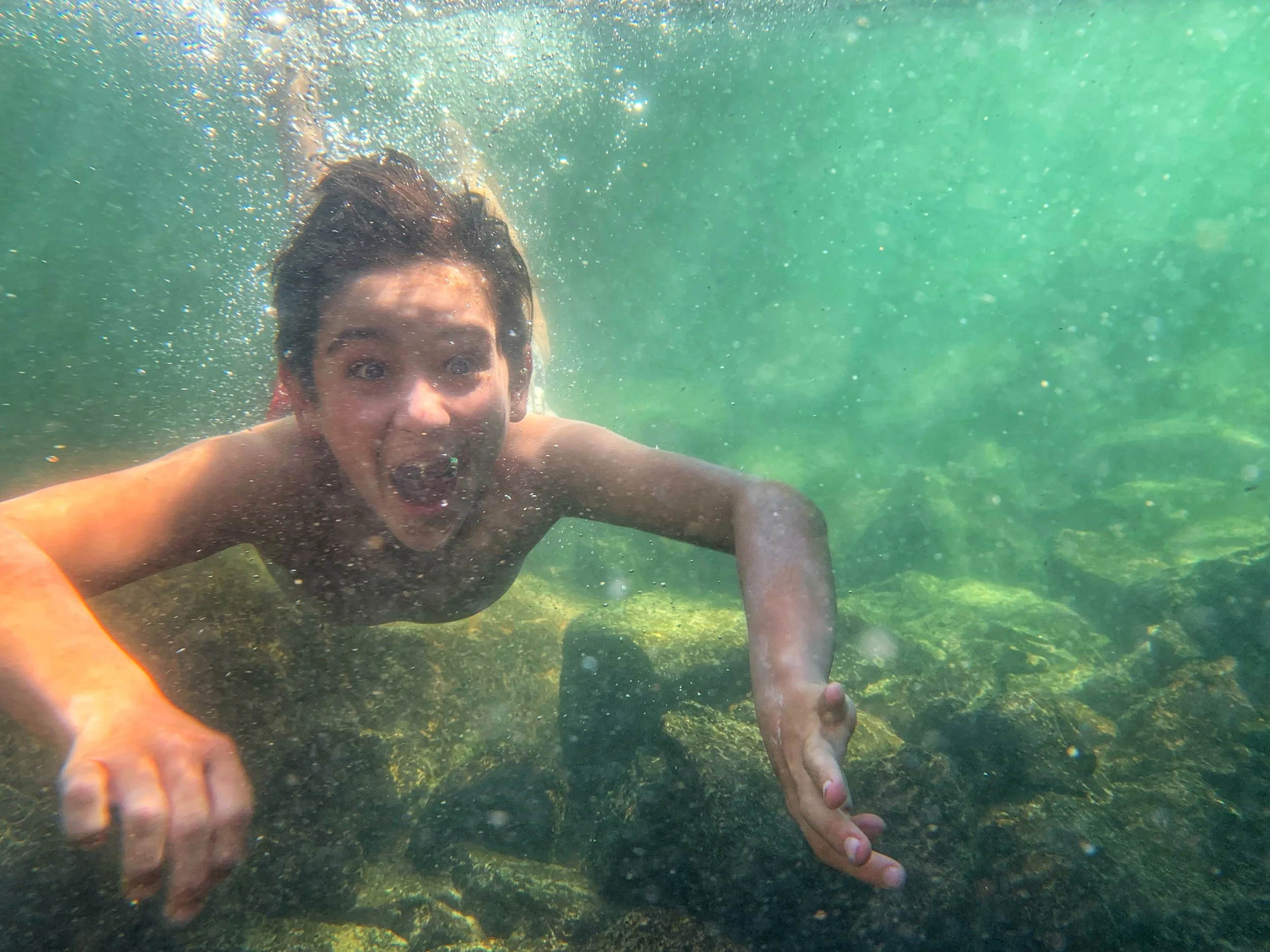 A young boy swims underwater with an expression of joy and wonder.