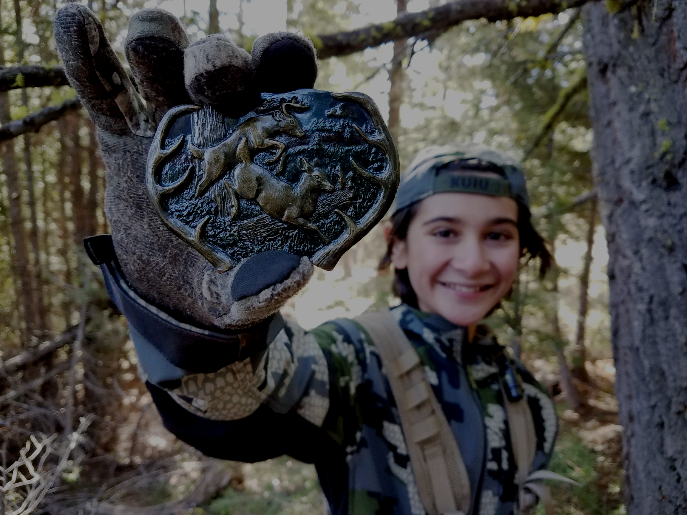 A boy in camouflage hunting with a belt buckle emblazoned with deer