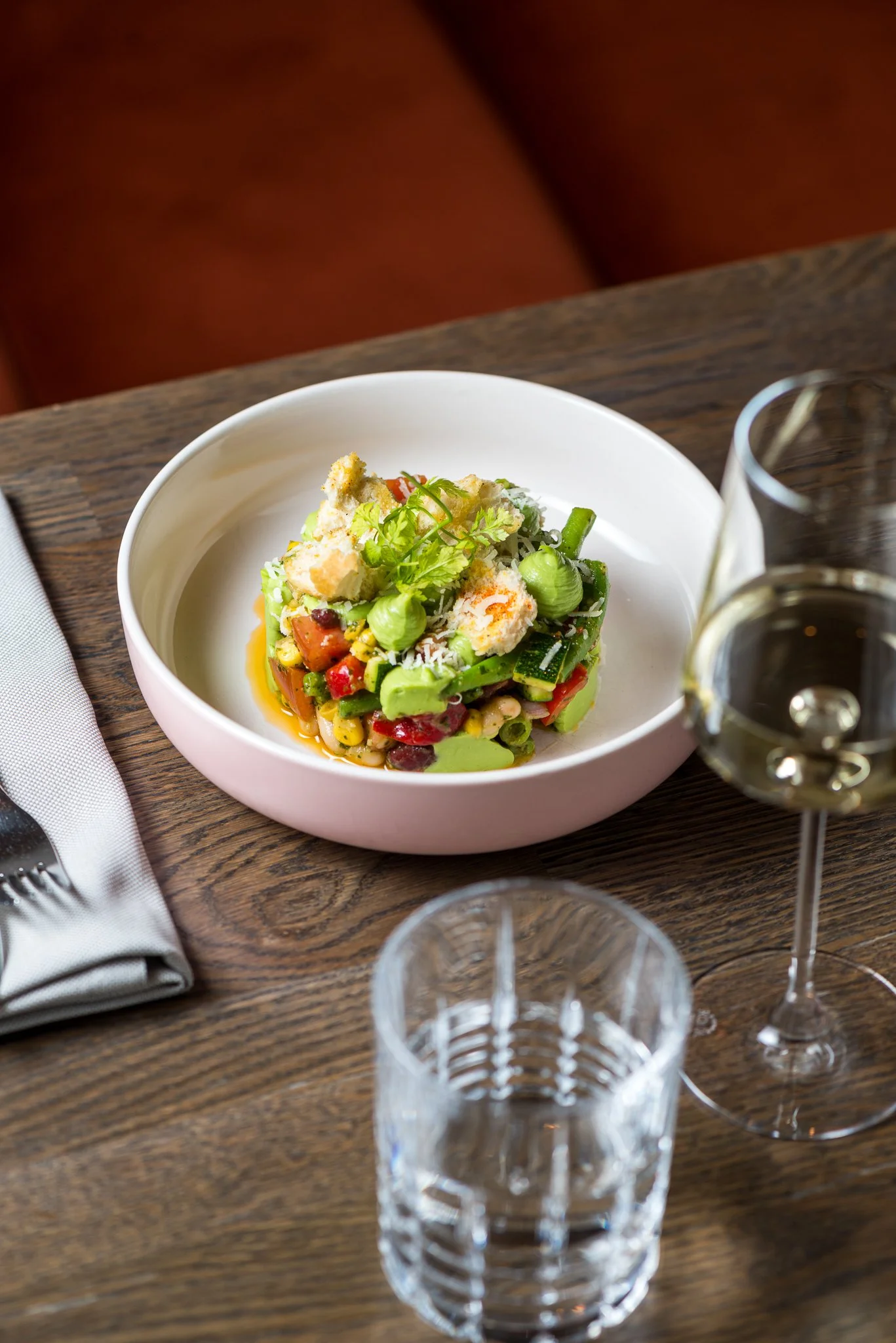 Gourmet vegetable salad in a bowl on a wooden table with a glass of white wine.