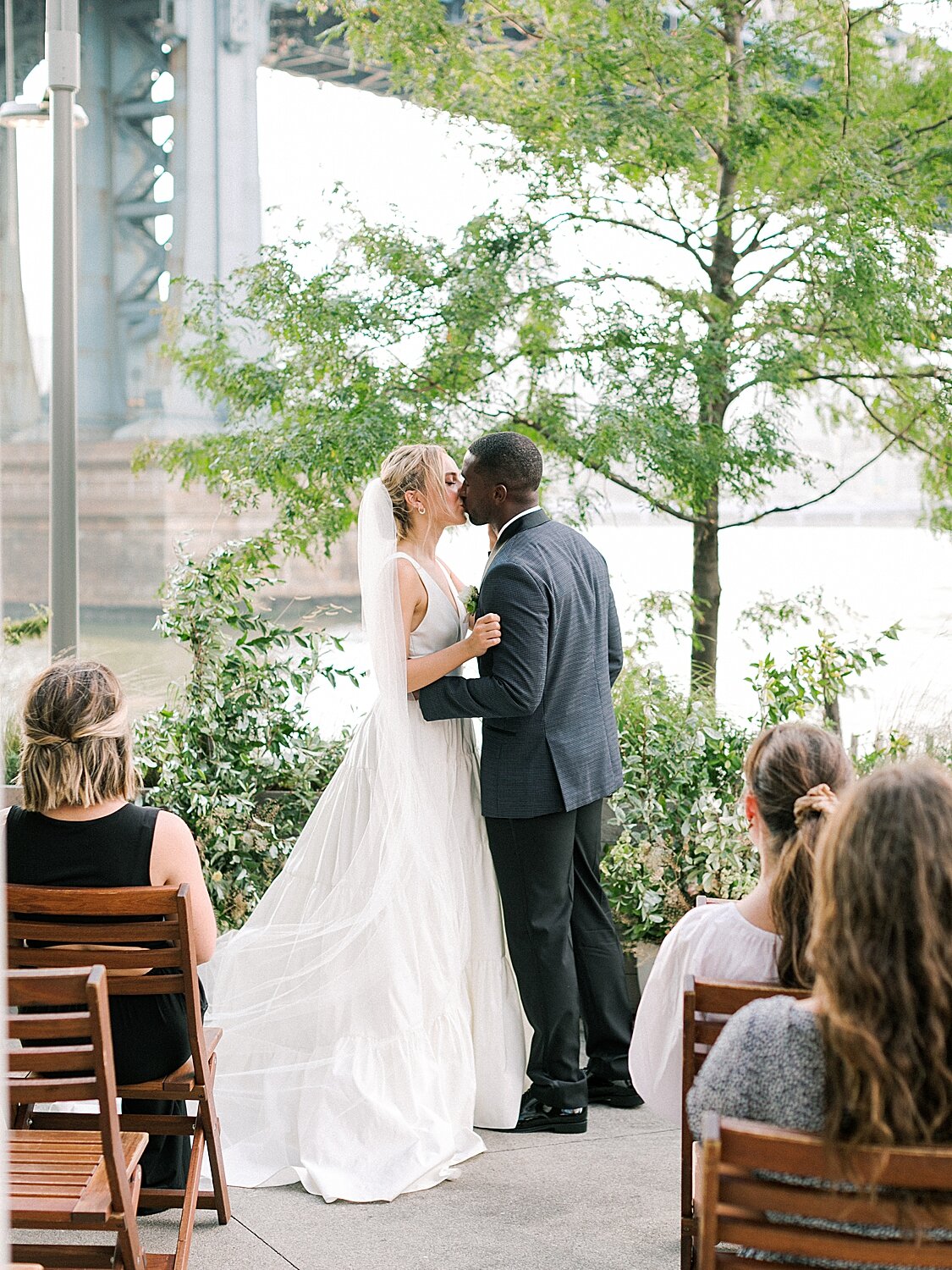 newlyweds kiss at Celestine with Brooklyn Bridge in distance | Asher Gardner Photography | Intimate Ceremony in DUMBO New York
