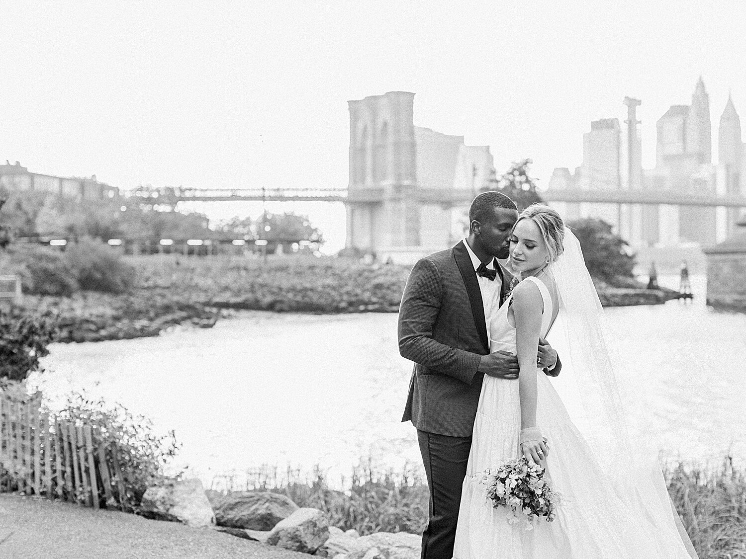newlyweds pose with New York skyline behind them | Asher Gardner Photography | Intimate Ceremony in DUMBO New York
