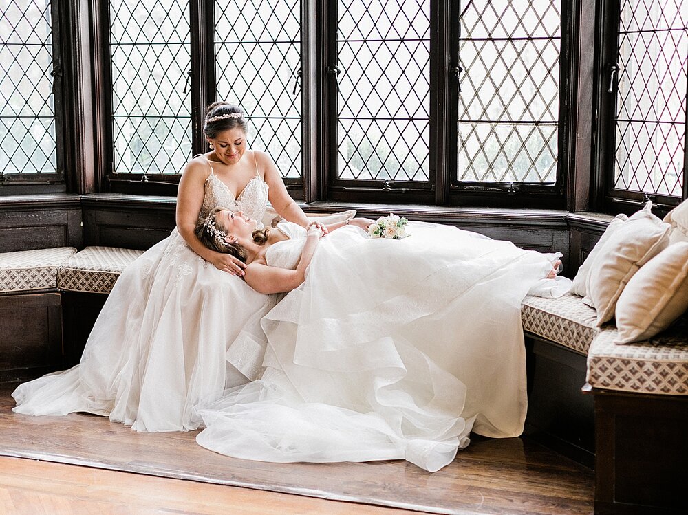bride lays on bride's lap sitting in window at Hempstead House during wedding portraits | Tri-State area wedding venues photographed by Asher Gardner Photography