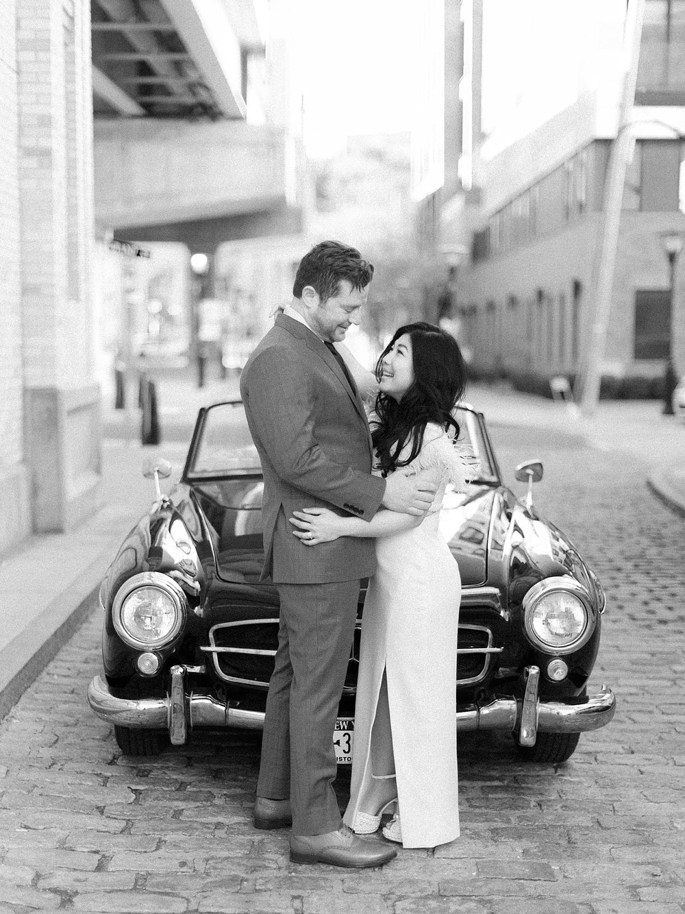 engaged couple stands in front of black classic Mercedes Benz 190sl hugging in New Jersey
