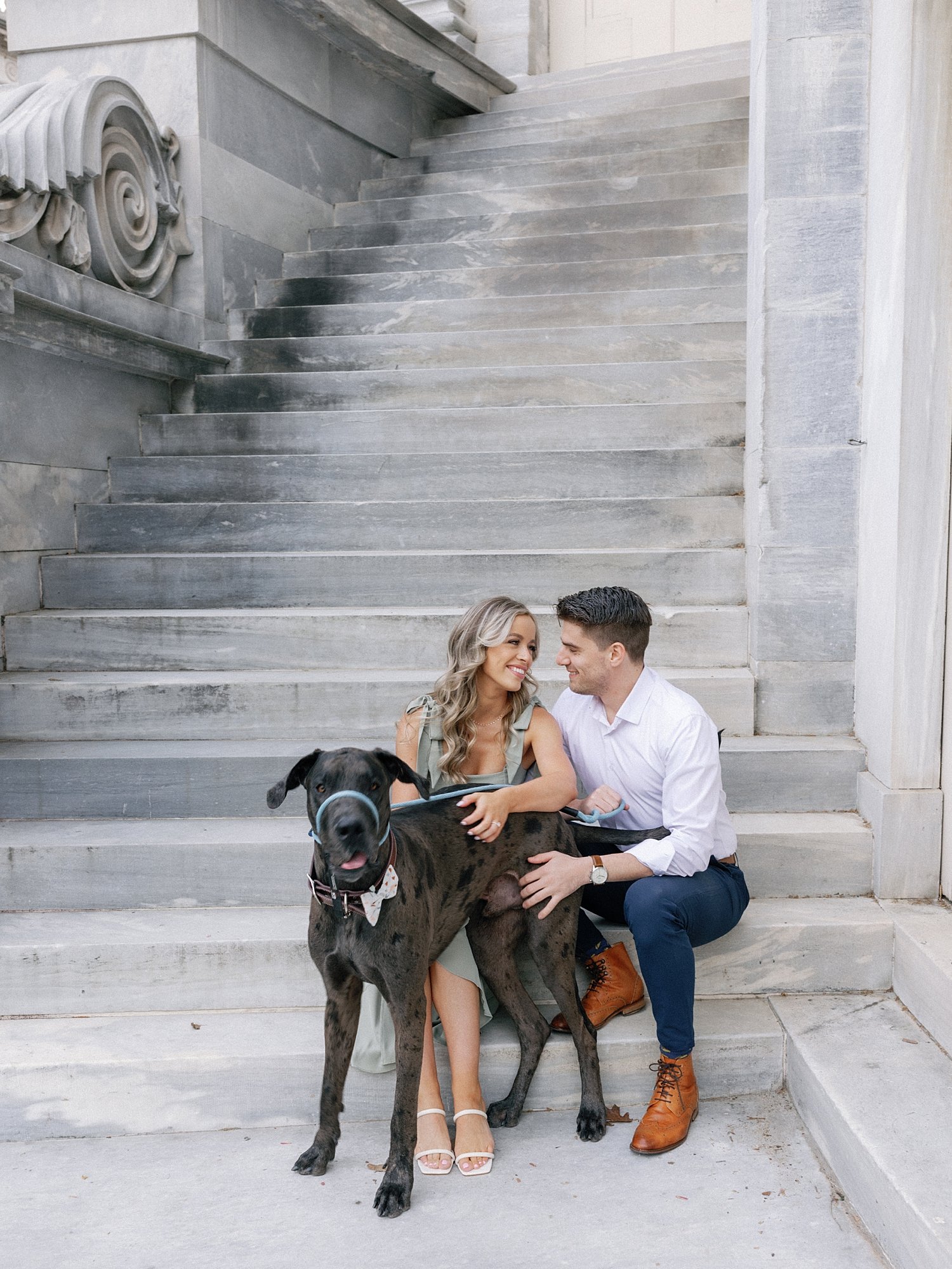 engaged couple sits on steps of the Merchant Exchange Building with Great Dane in Philly PA